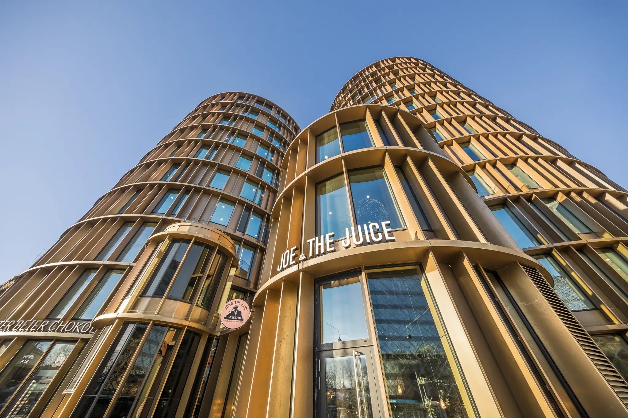 Dobbelte guldbegejrede bygninger med Joe & The Juice-skilt og vinduer mod skyen