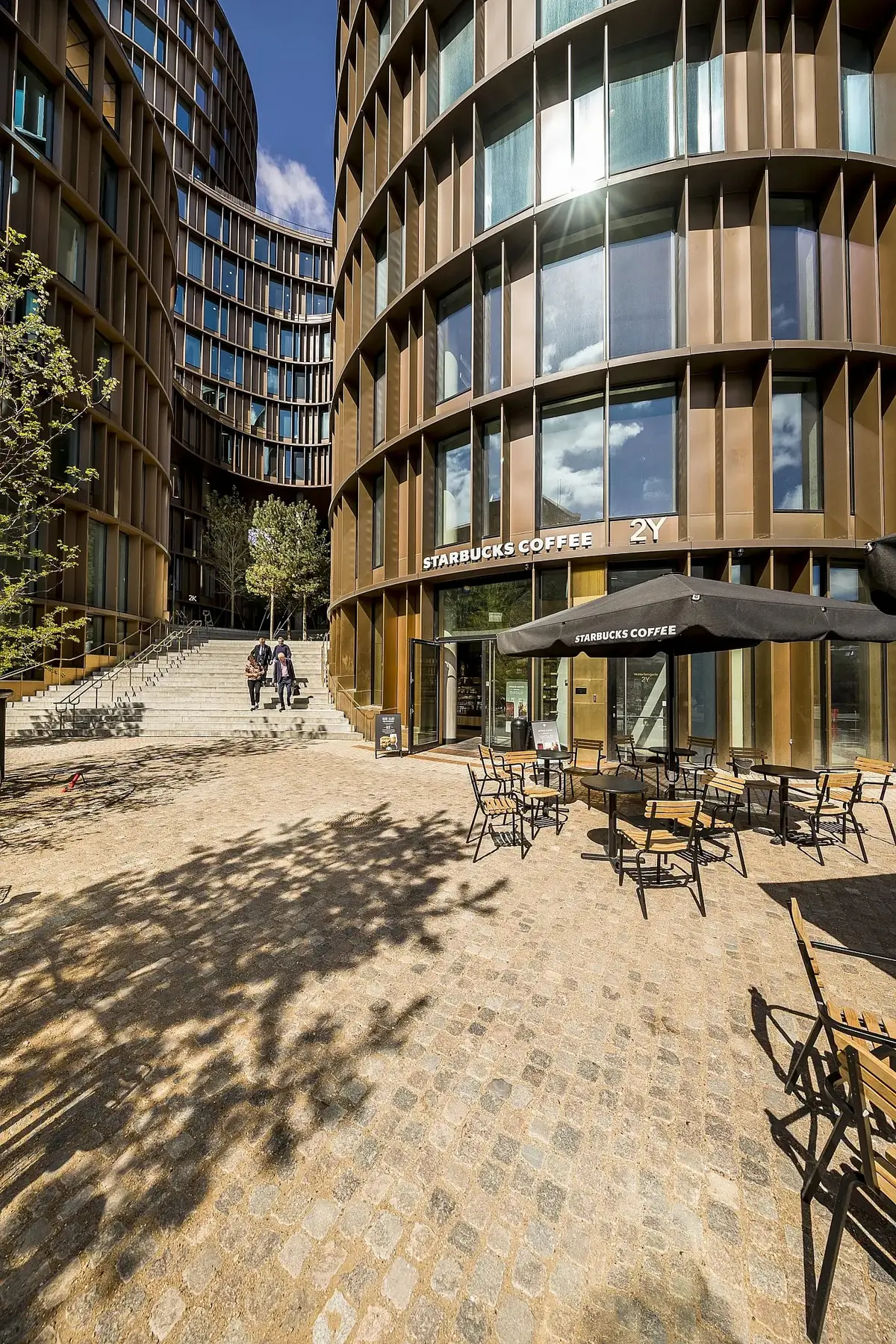 Moderne bygninger med Starbucks Coffee på 2Y, med et bord og en parasol uden for og folk, der går op ad trappen