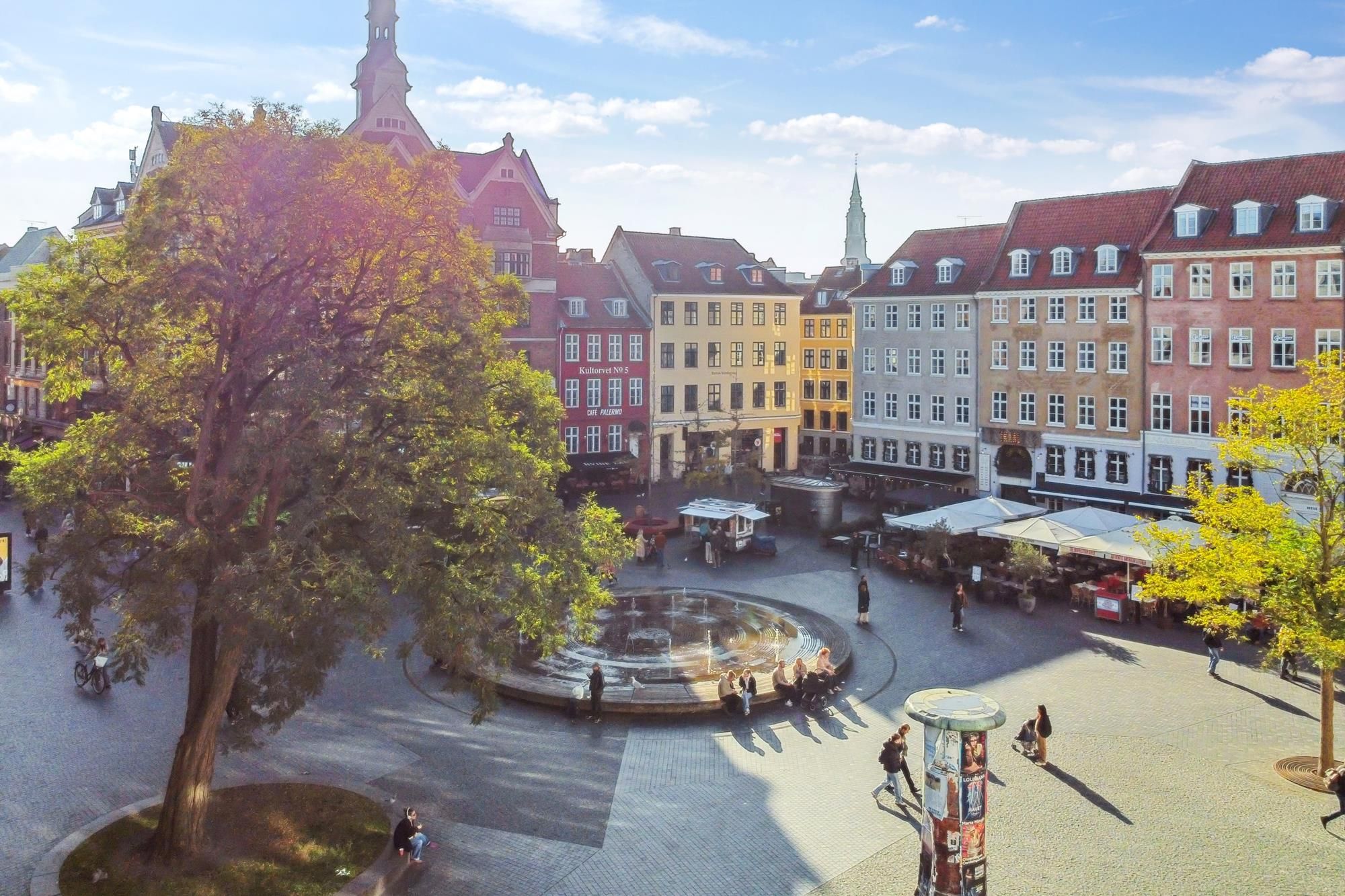 En turister i en by med små butikker og caféer rundt omkring Hauser Plads i København.