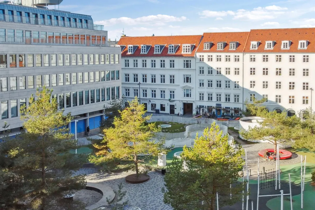 Kontorbyggeri med park og skulpturer på Hauser Plads, to huse med røde tag og mange vinduer