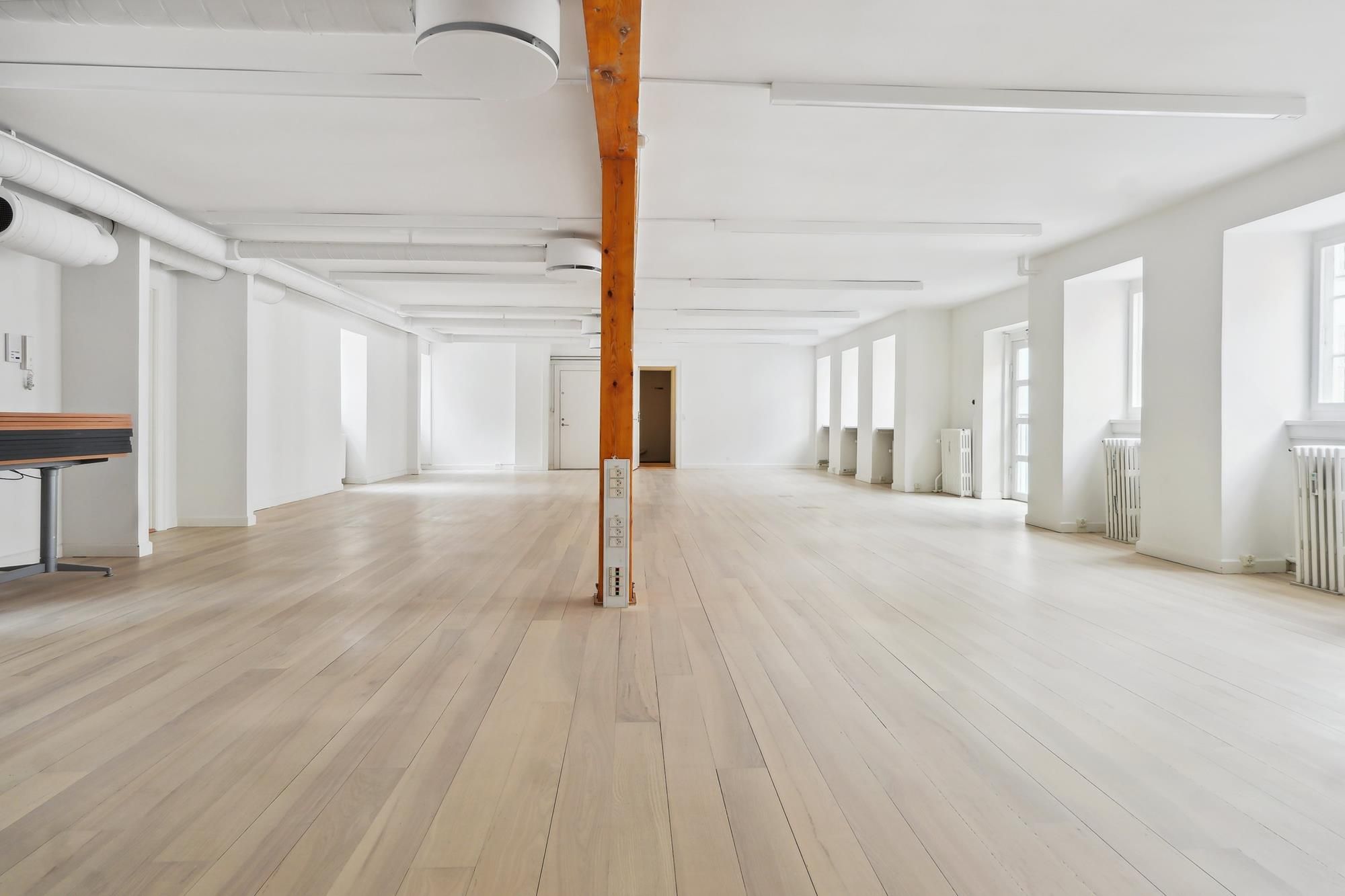 Lys interiør med hvide vægge og loft, lysegrå gulvbelægning og åbne vinduer med hvide ruder