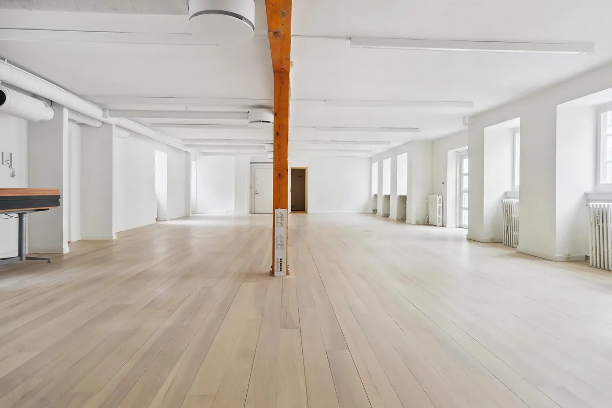 Lys interiør med hvide vægge og loft, lysegrå gulvbelægning og åbne vinduer med hvide ruder