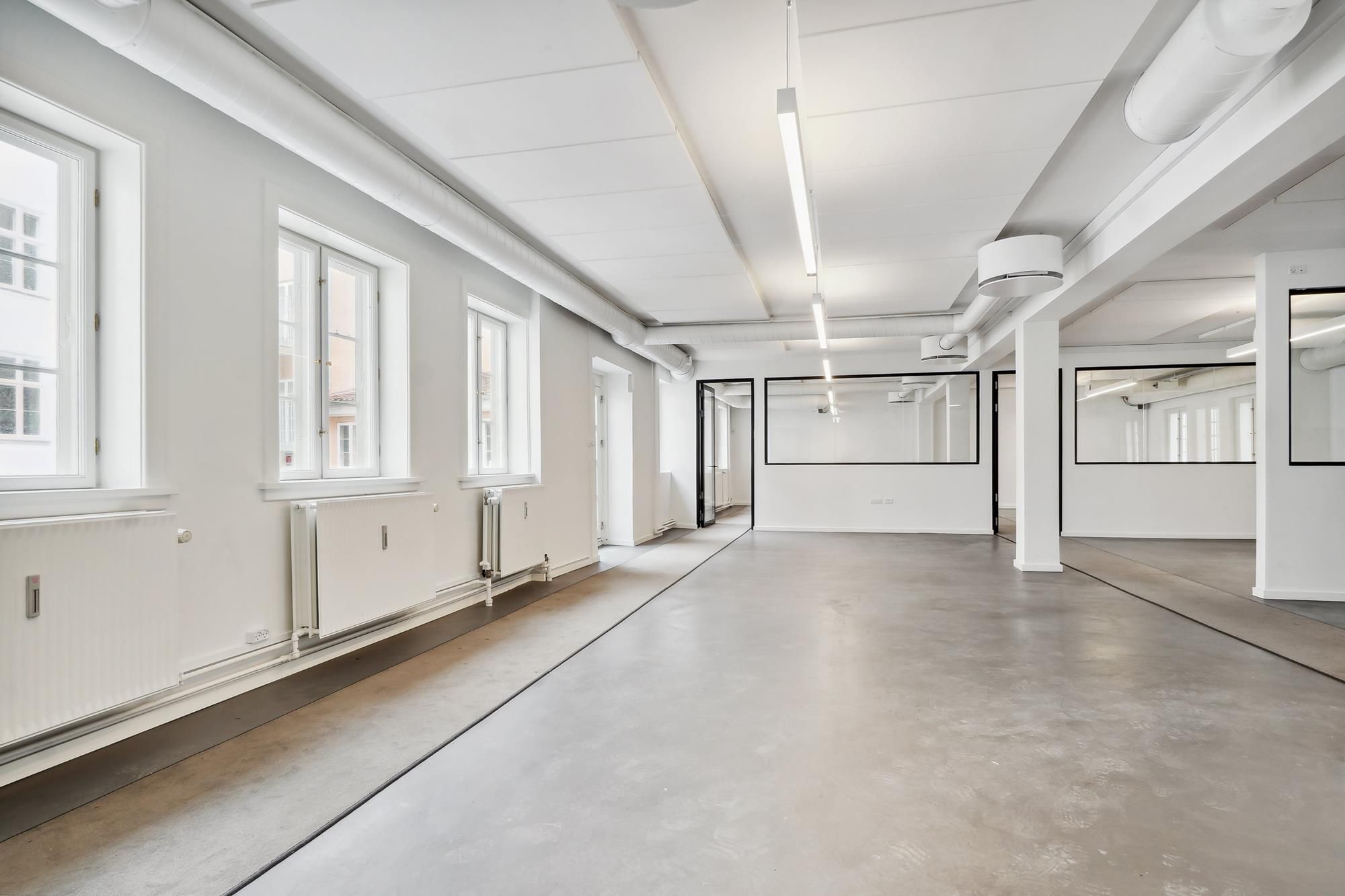 Ledig og nyrenoveret kontor i et bygningsfelt med lyseruder og spejl og møbler i hvidt