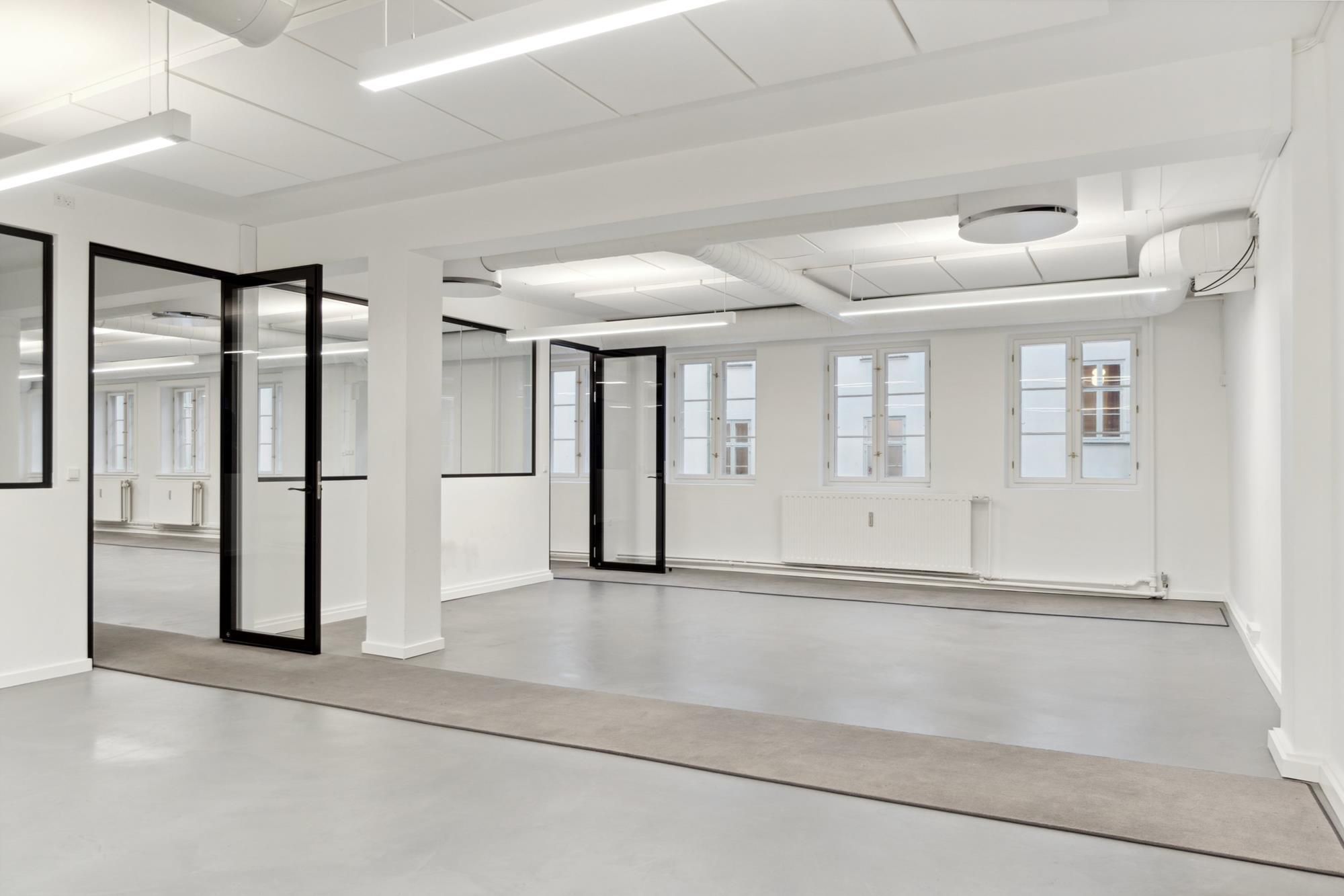 Moderne kontor med hvide vægge, glasdøre, gulvbelægning og store vinduer med udsigter til byen