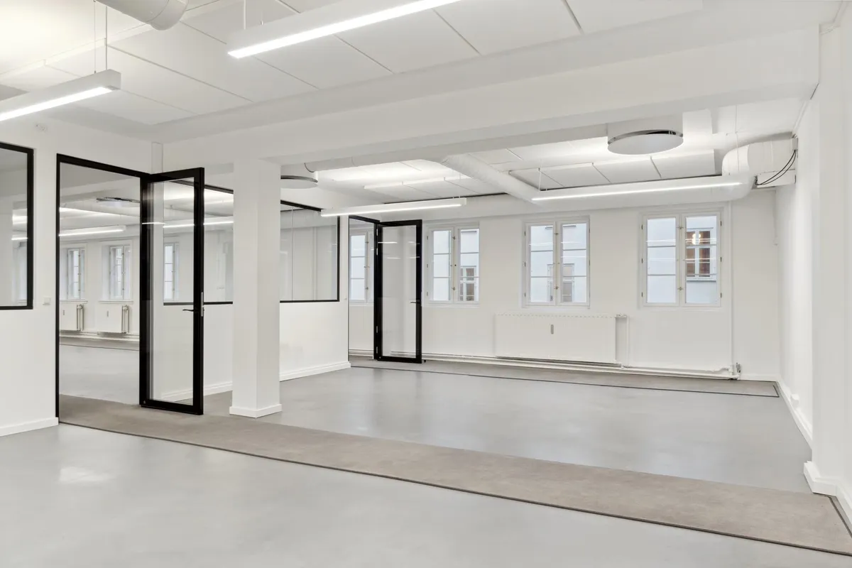 Moderne kontor med hvide vægge, glasdøre, gulvbelægning og store vinduer med udsigter til byen