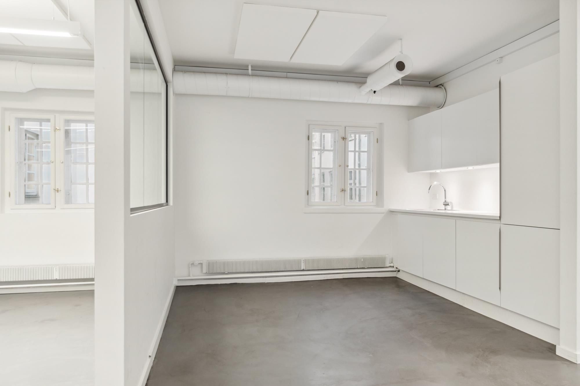 Et tomt kontor med hvide vægge og gulve, hvidt loft, en radiator og to vinduer med hvide ruder