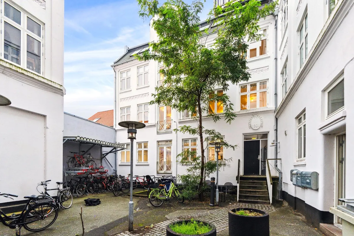 Lyst og indbydende kontor i Aarhus med lyse vinduer, smukke træer og parkerede cykler i gaden.