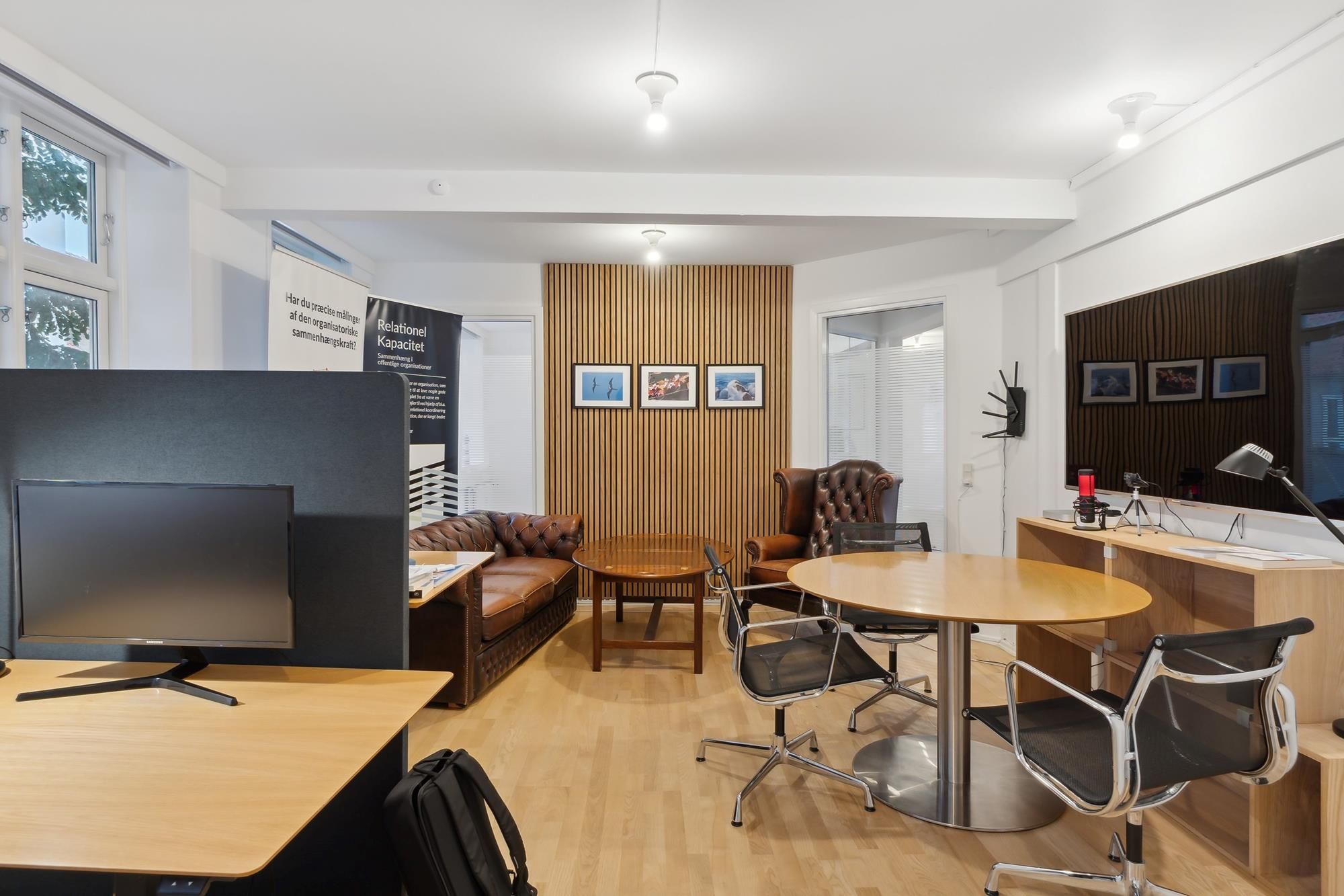 Lyst og indbydende kontor med lyse gulvvægge, runde borde og moderne møbler. Tre billeder hænger på væggen og der er en stor