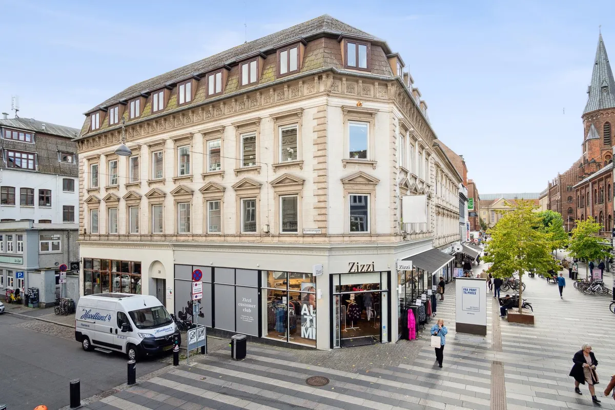 Vandret parkerede hvid lastbil foran Zizzi, mens folk går på gågaden, og gamle bygninger og kirker ligger i baggrunden