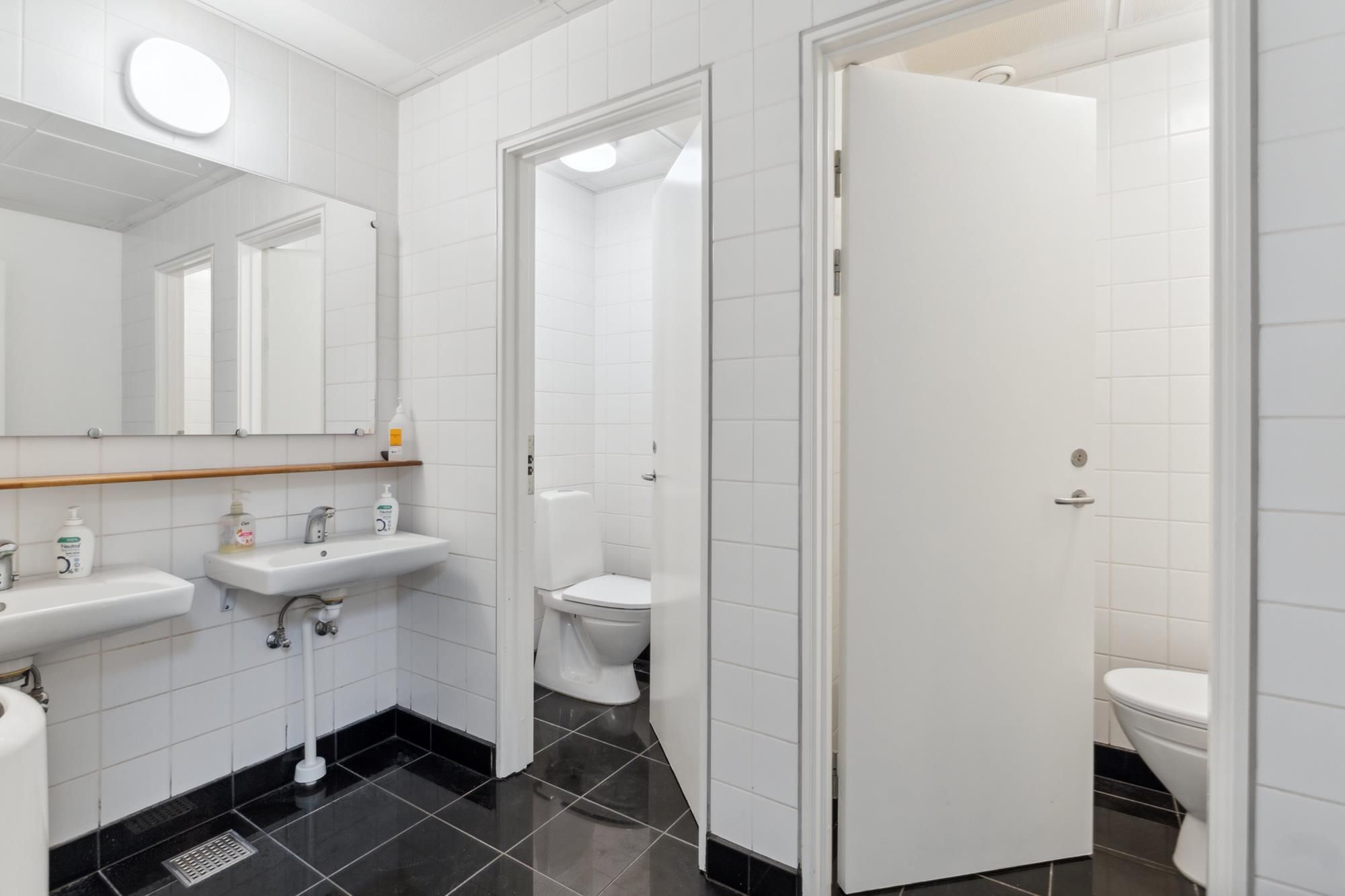 Lyst og åbent badeværelse med toilet, to vasker og et spejl i hvidt og sort interiør