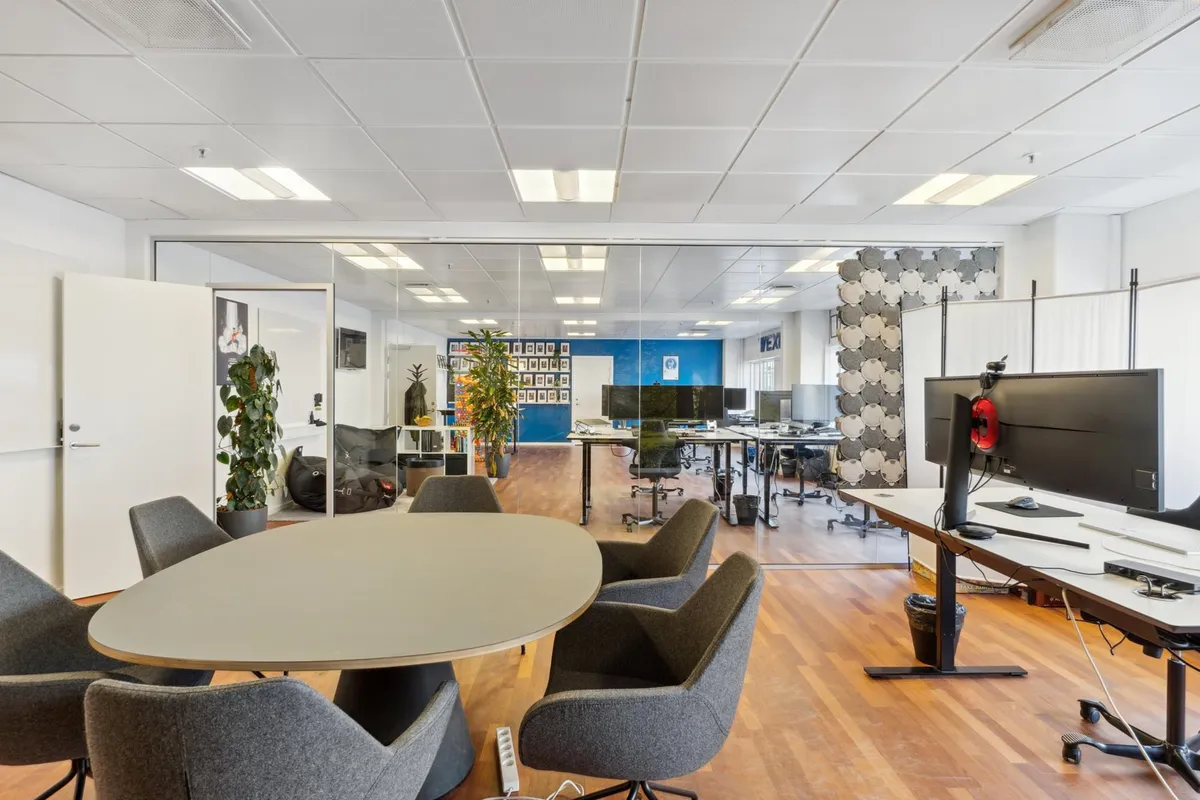 Lyst og åbent kontor med trægulve, runde skriveborde, lyse vinduer og enkelt kontormøbler