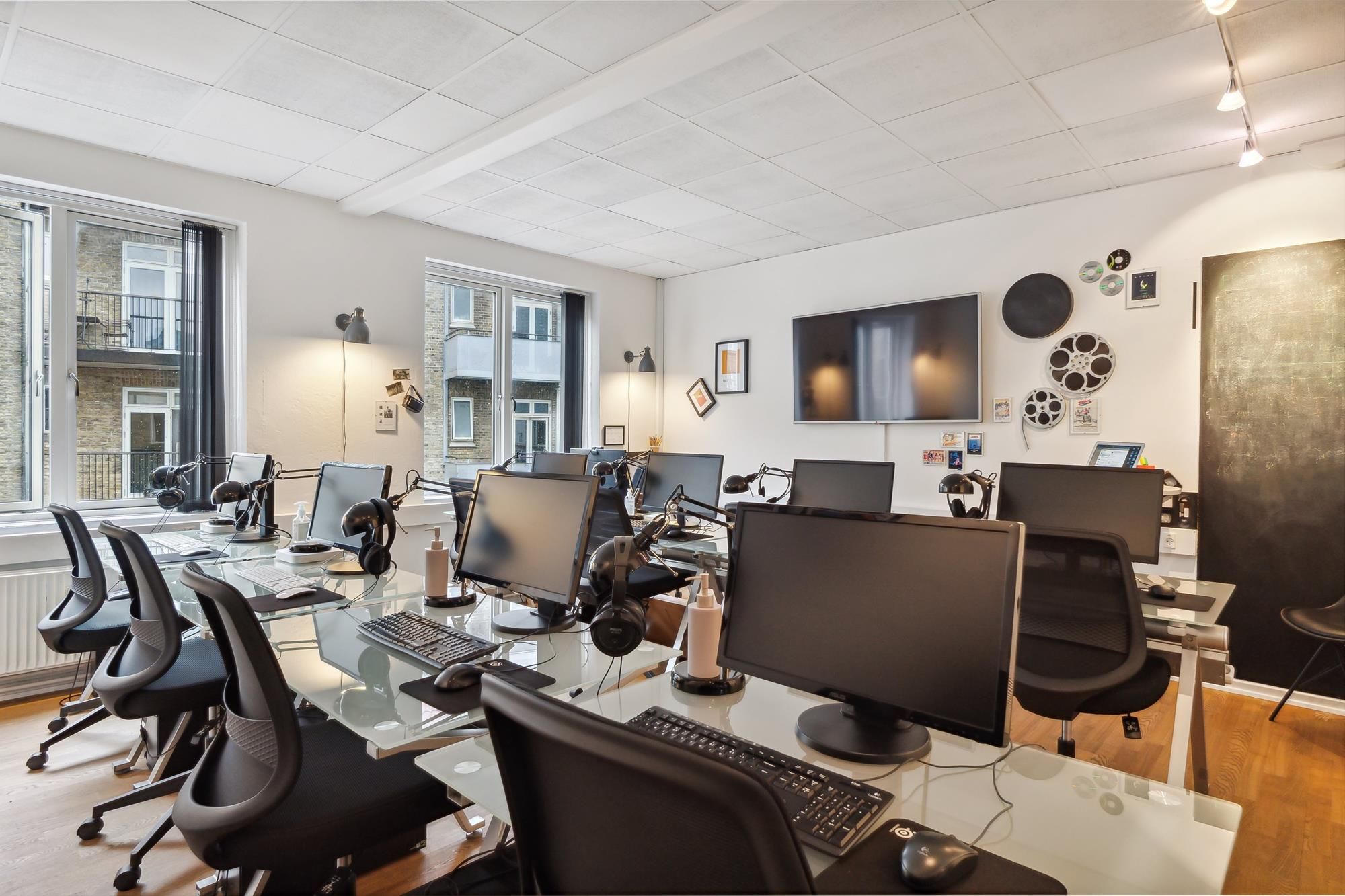 Mange computere og skriveborde med højtalere i et velindrettet kontor med højt til loftet