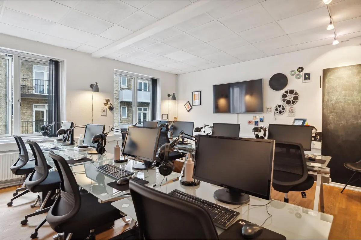 Mange computere og skriveborde med højtalere i et velindrettet kontor med højt til loftet