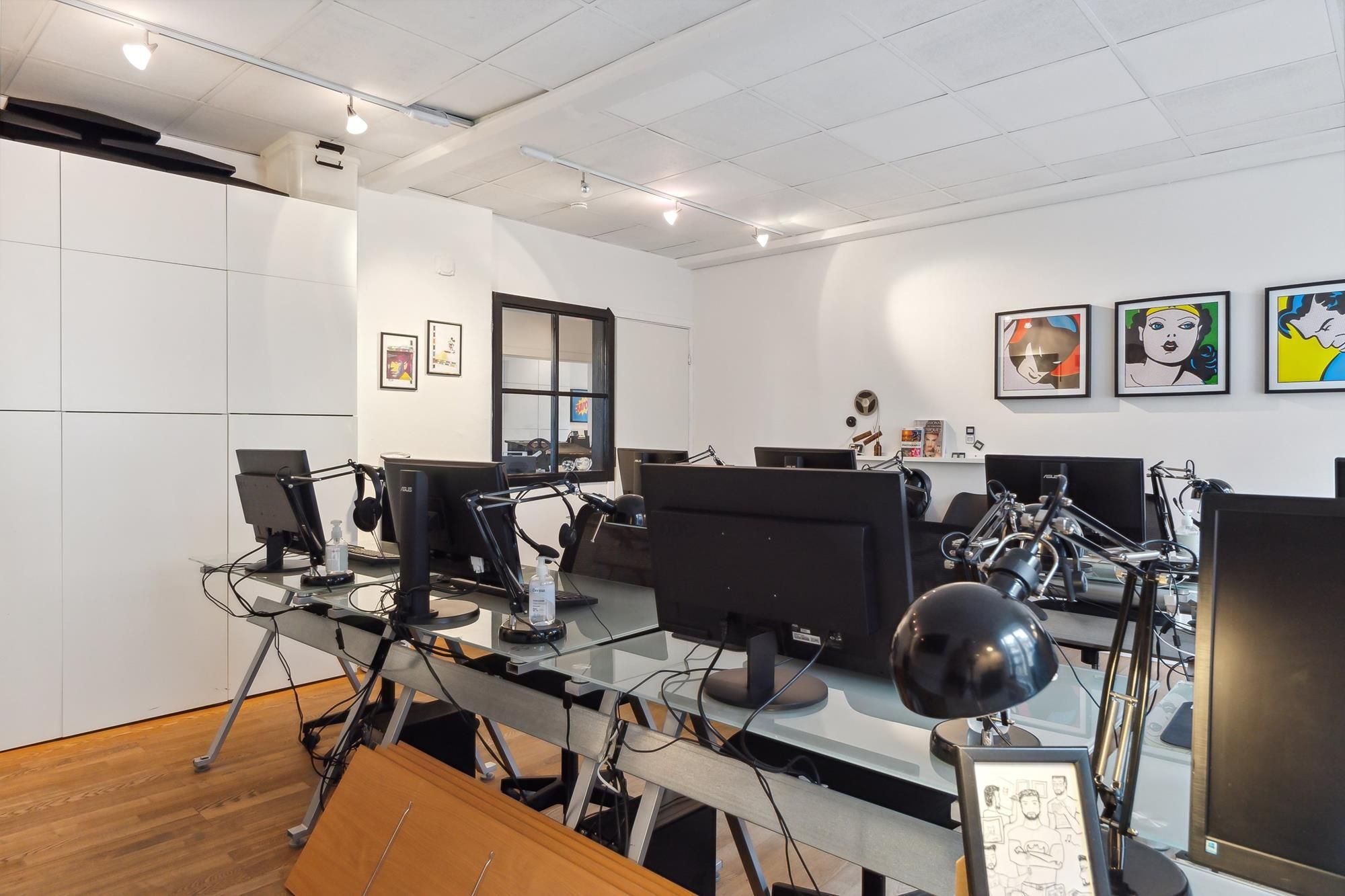 Lejemål med moderne computere, skærme og lyse lamper. Der er billeder på væggen og hylder med diverse genstande