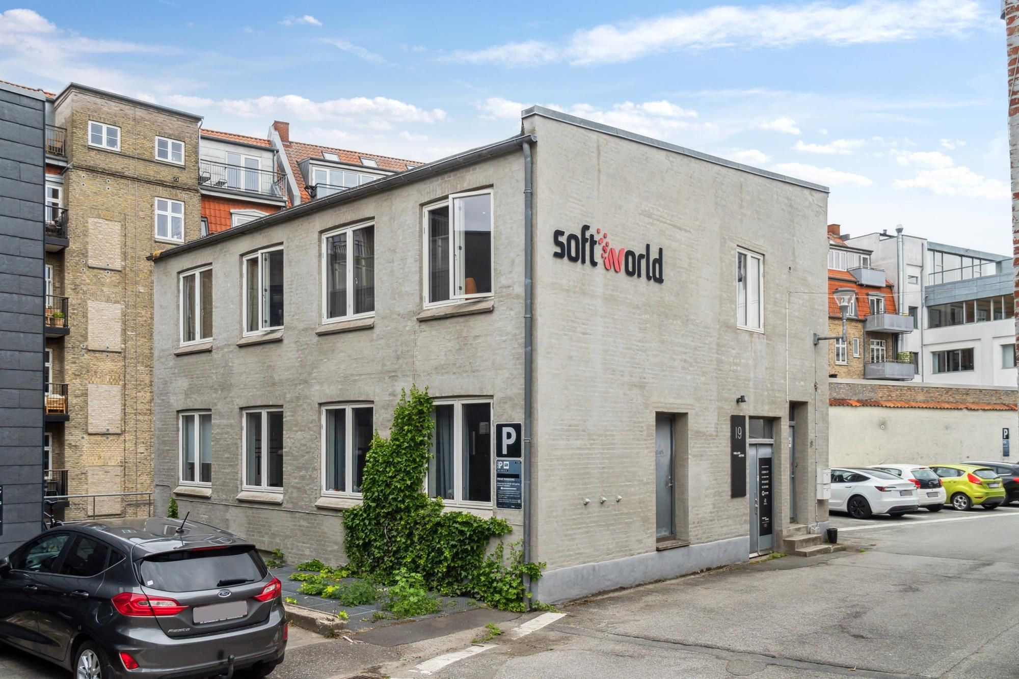 Kontorbyggeri med teksten Soft World, hvor der står parkeringsskilt med P og biler parkeret på siden af bygningen