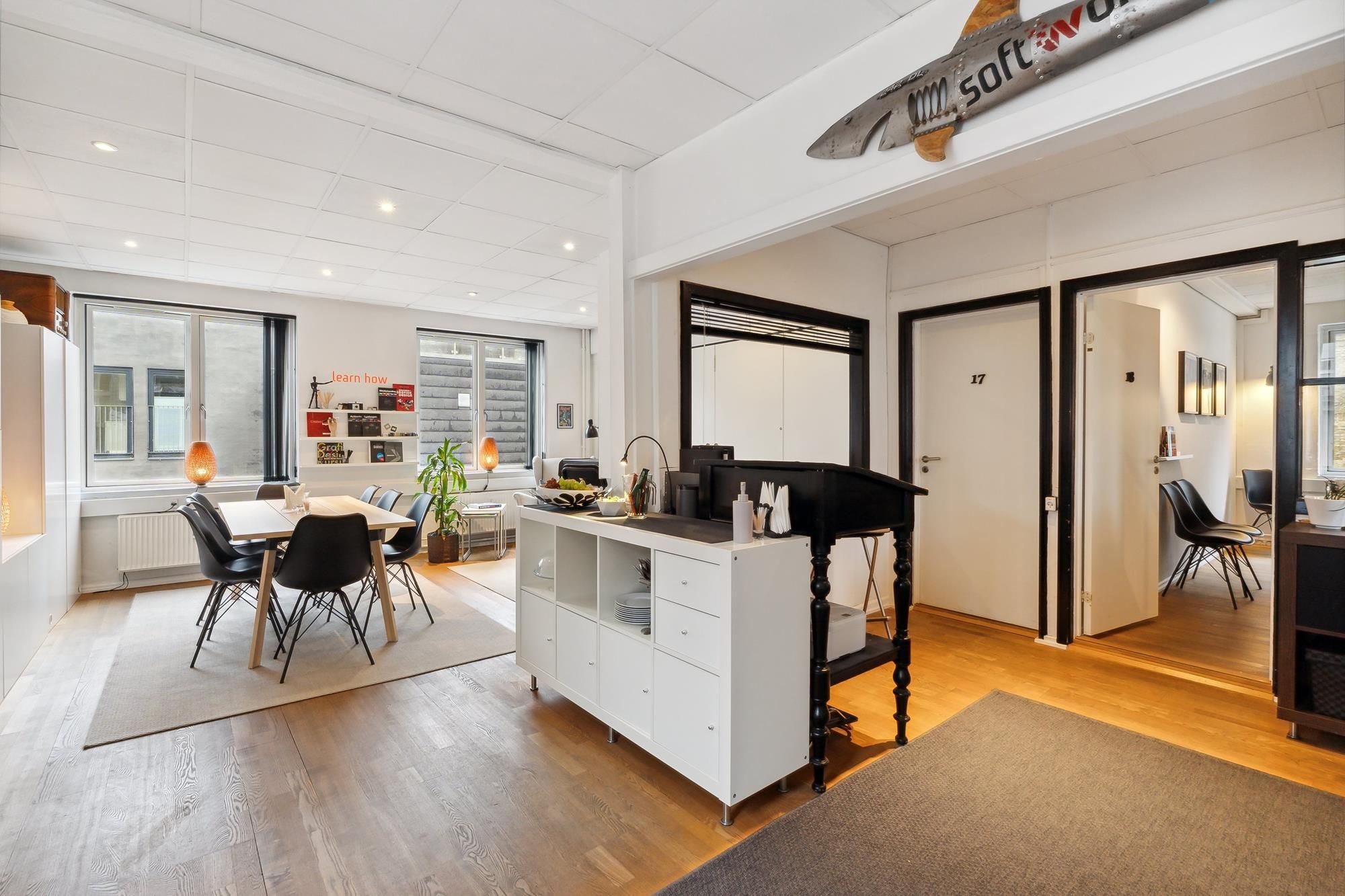 Lejlighed med køkken og spiseplads samt trægulv og hvide vægge med store vinduer