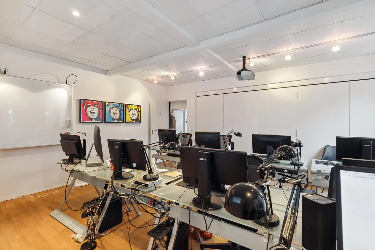 Et studieværelse med mange computere, en hvid tavle og fire farverige malerier på væggen