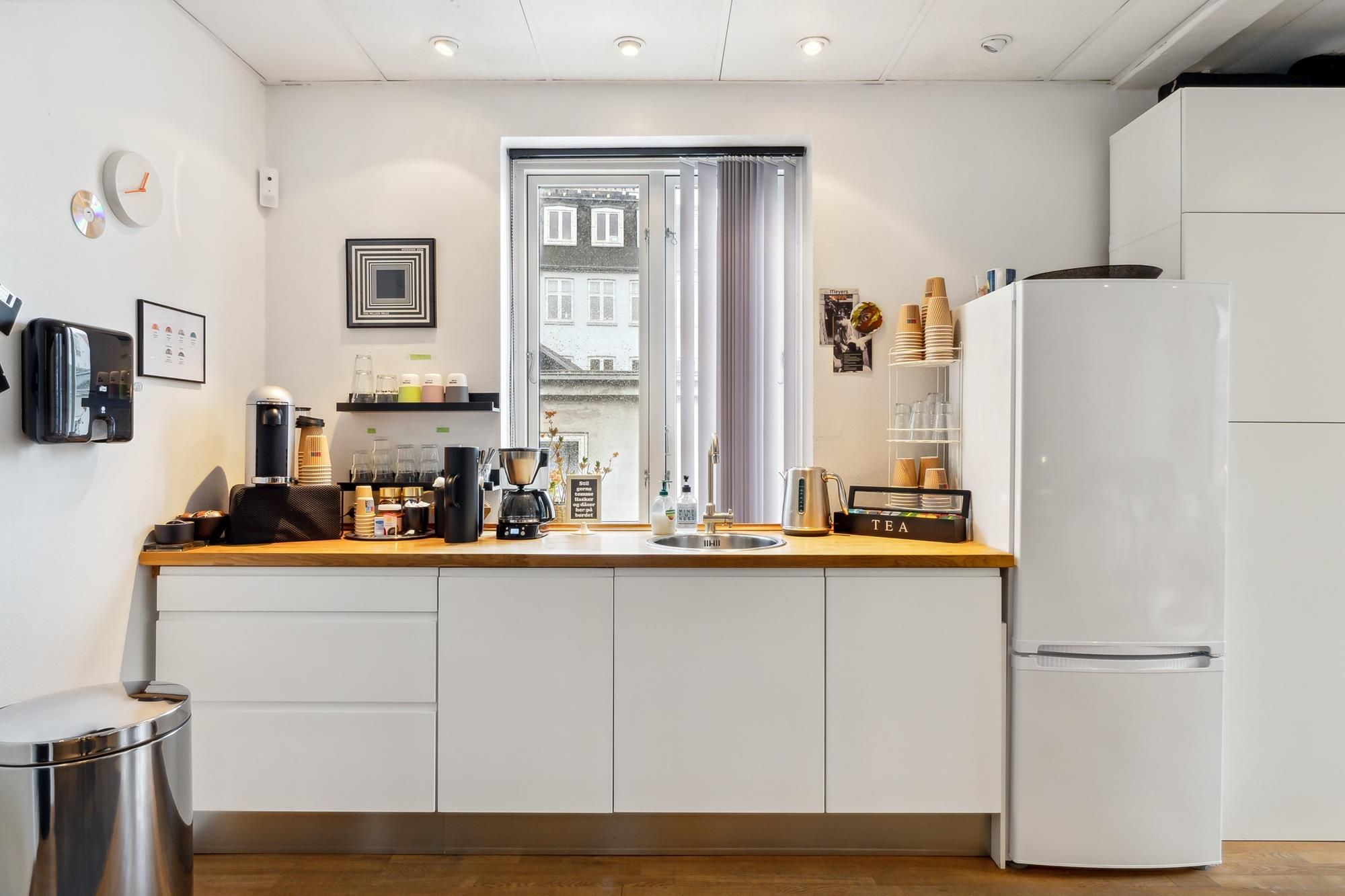 En hvid køkken med lysegult træarbejde og hvide hylder samt en køleskab, en ovn og en mikrobølgeovn