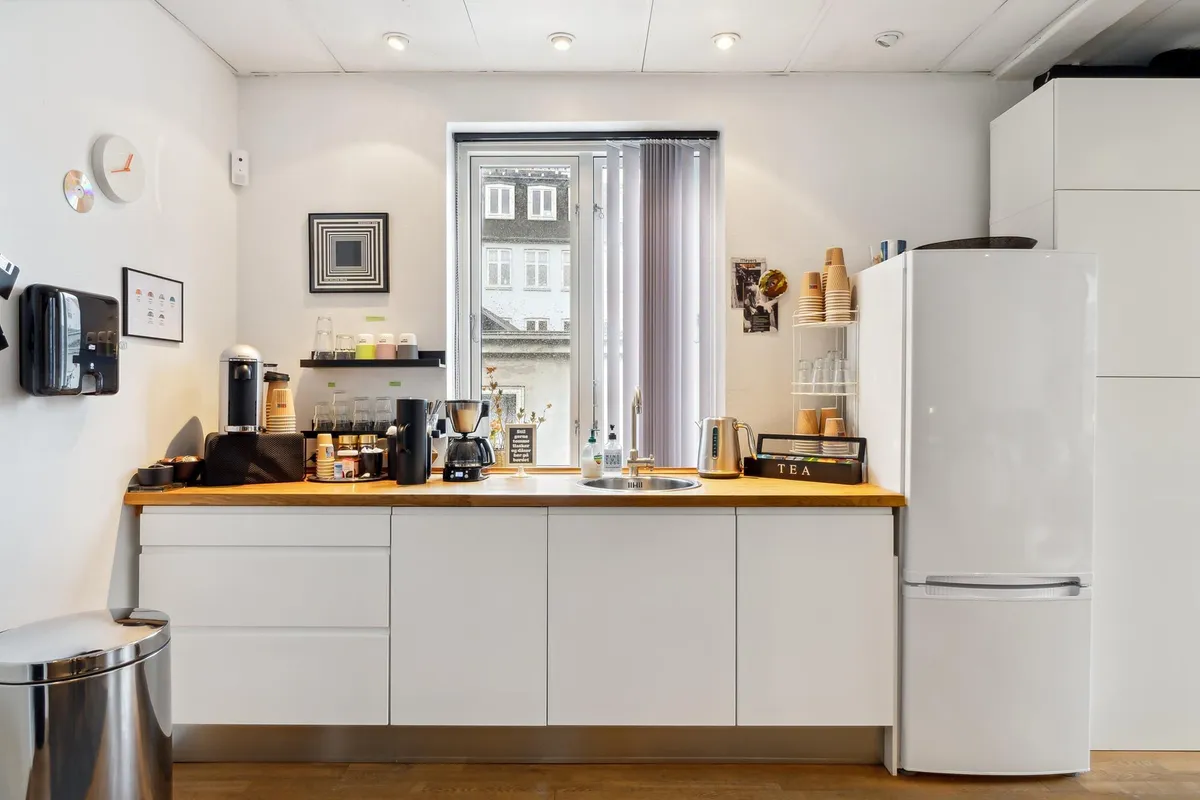 En hvid køkken med lysegult træarbejde og hvide hylder samt en køleskab, en ovn og en mikrobølgeovn