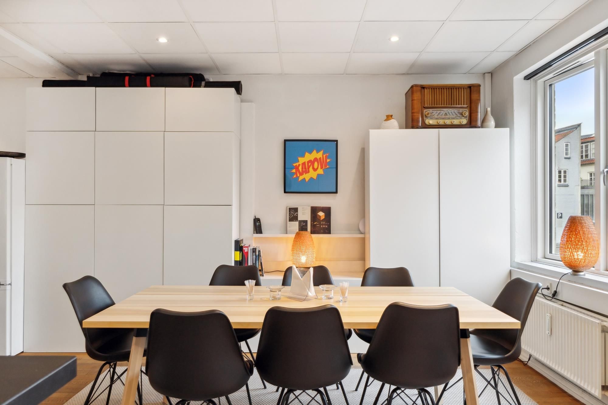 Lyst og moderne køkken med højloft og lyse lamper samt bord og stole samt flotte møbler og loftsrum med kommoder og vindue