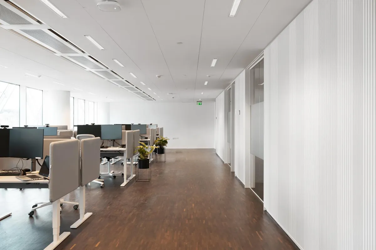 Kontorlokaler med højt til loftet, moderne møbler, og et minimalistisk design med hvide vægge og trægulve