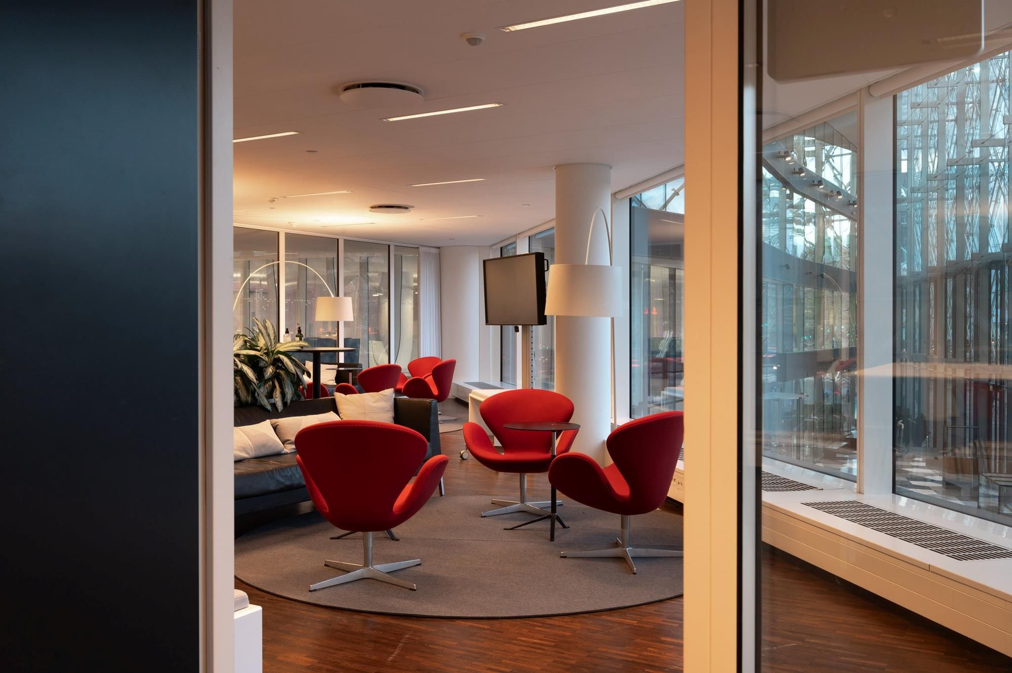 Kontorlokaler med røde stole, højtloft, gulvtæppe, sofa, tv, skrivebord, plante og lysekroner i en moderne indretning