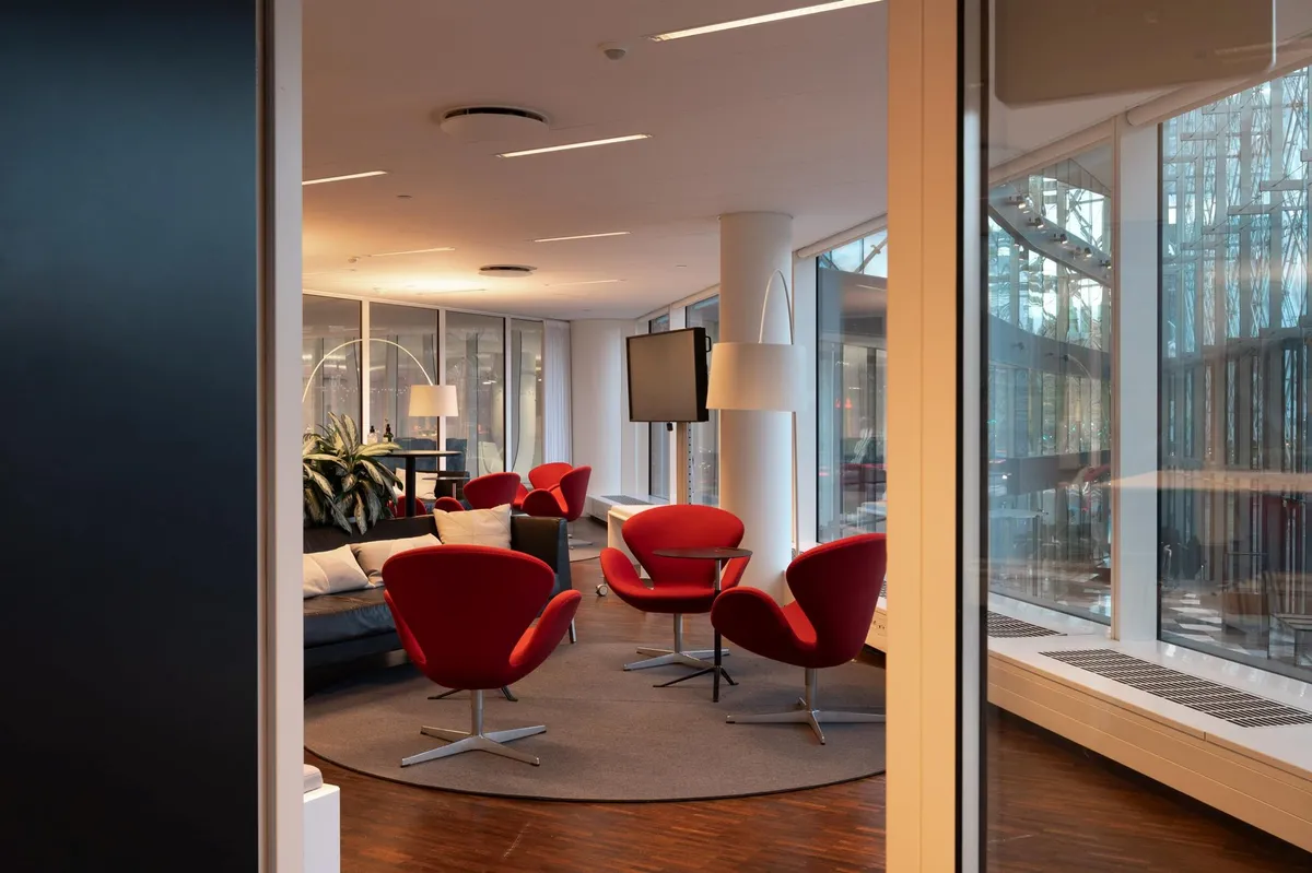 Kontorlokaler med røde stole, højtloft, gulvtæppe, sofa, tv, skrivebord, plante og lysekroner i en moderne indretning