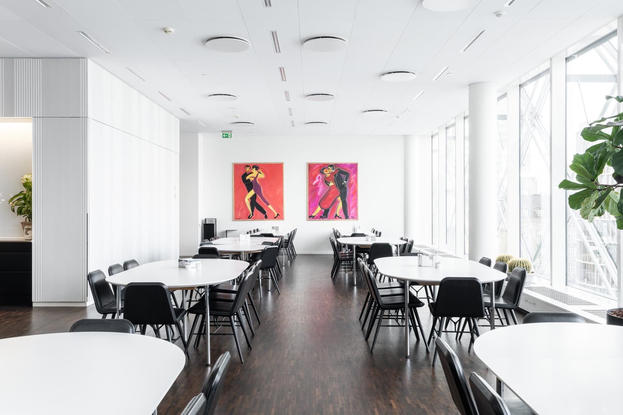 Kontorlokaler med runde hvide borde og stole, malerier og plantepot med en kaktus i en hjørne.