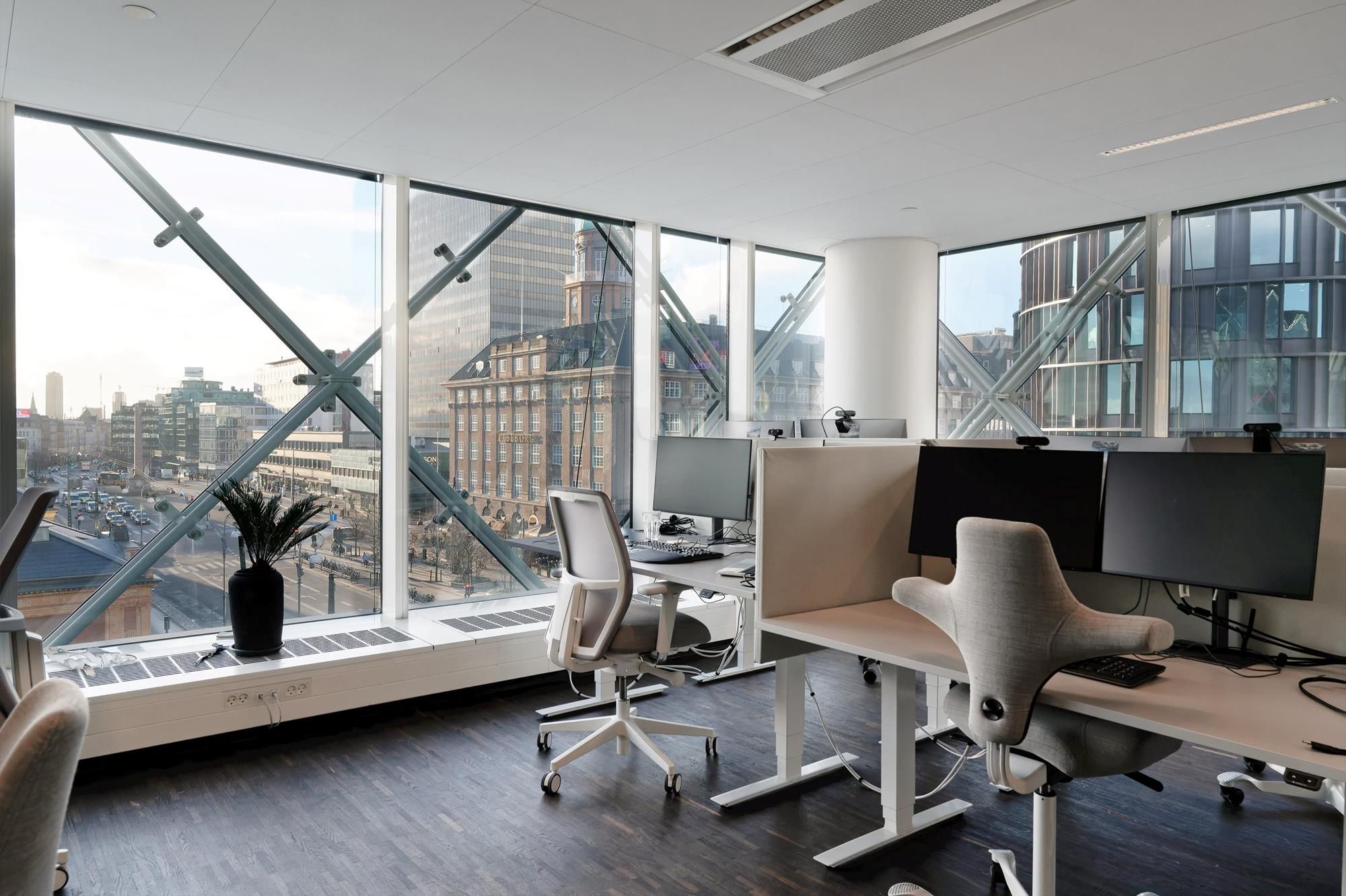 Kontor med udsigter over byen fra store vinduer og moderne kontormøbler med flere skærme og skriveborde