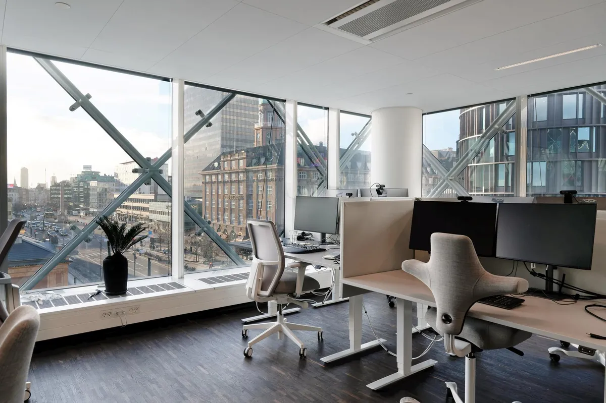 Kontor med udsigter over byen fra store vinduer og moderne kontormøbler med flere skærme og skriveborde