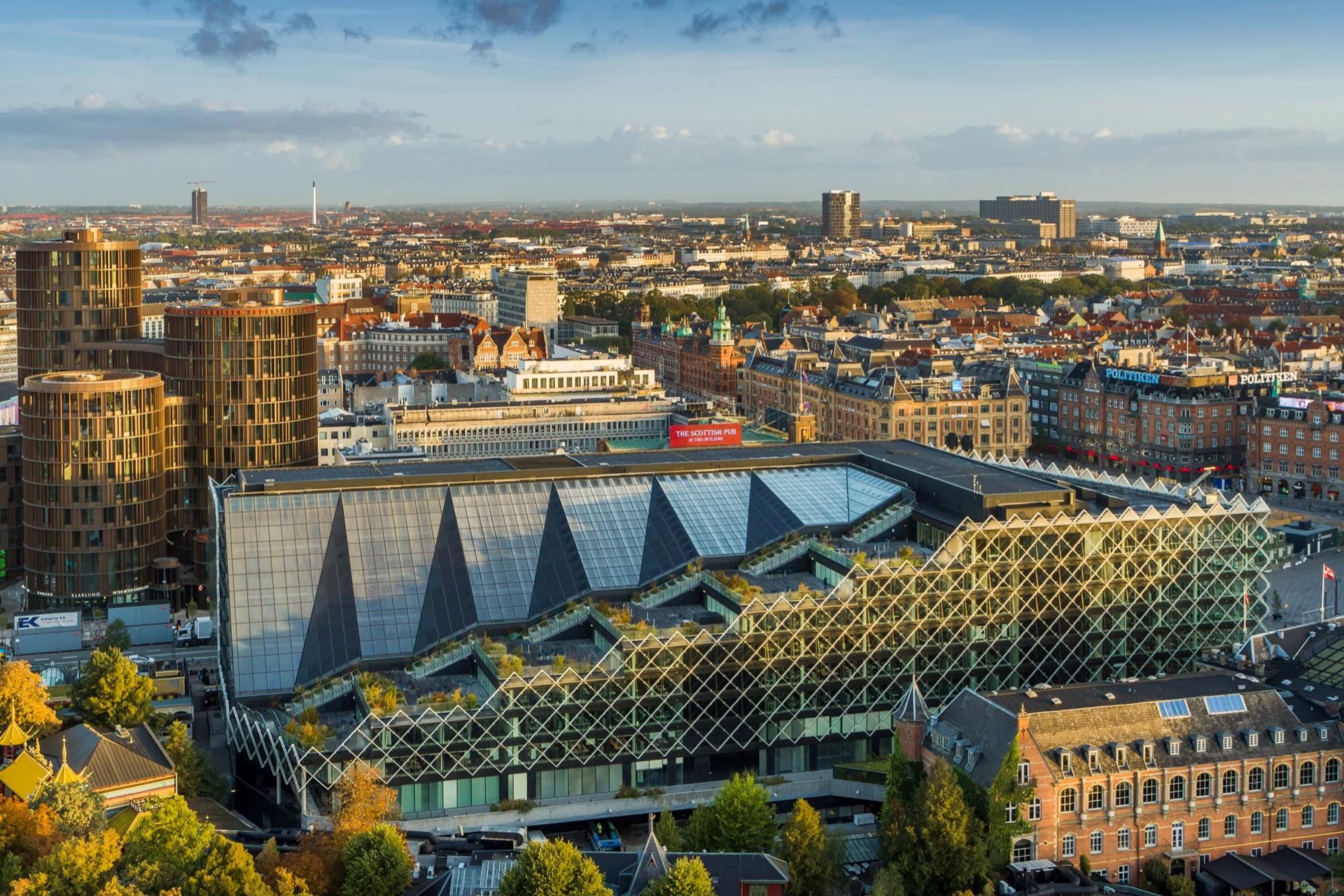 Byens skyline med høje bygninger og grønne træer, hvor det imponerende Industriens Hus står frem med sit unikke design og