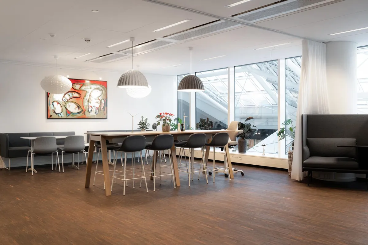 Moderne kontorlokaler med lyse loftslamper, stort vinduesparti, kunstværk, møbler og planter tilføjer en hyggelig atmosfære