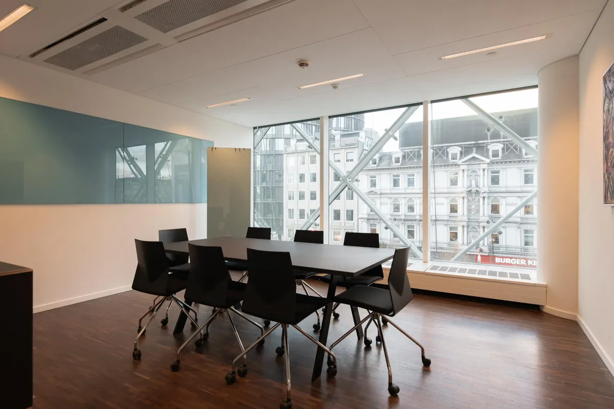 Kontorrum med møbelsæt, store vinduer med udsigt til bygning og Burger King-reklame, lysegult vægpanel og trægulv