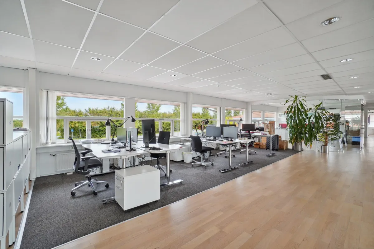Moderne og flot erhvervspark med lyse kontorer, computere og møbler samt vinduer med udsigt til grønne træer