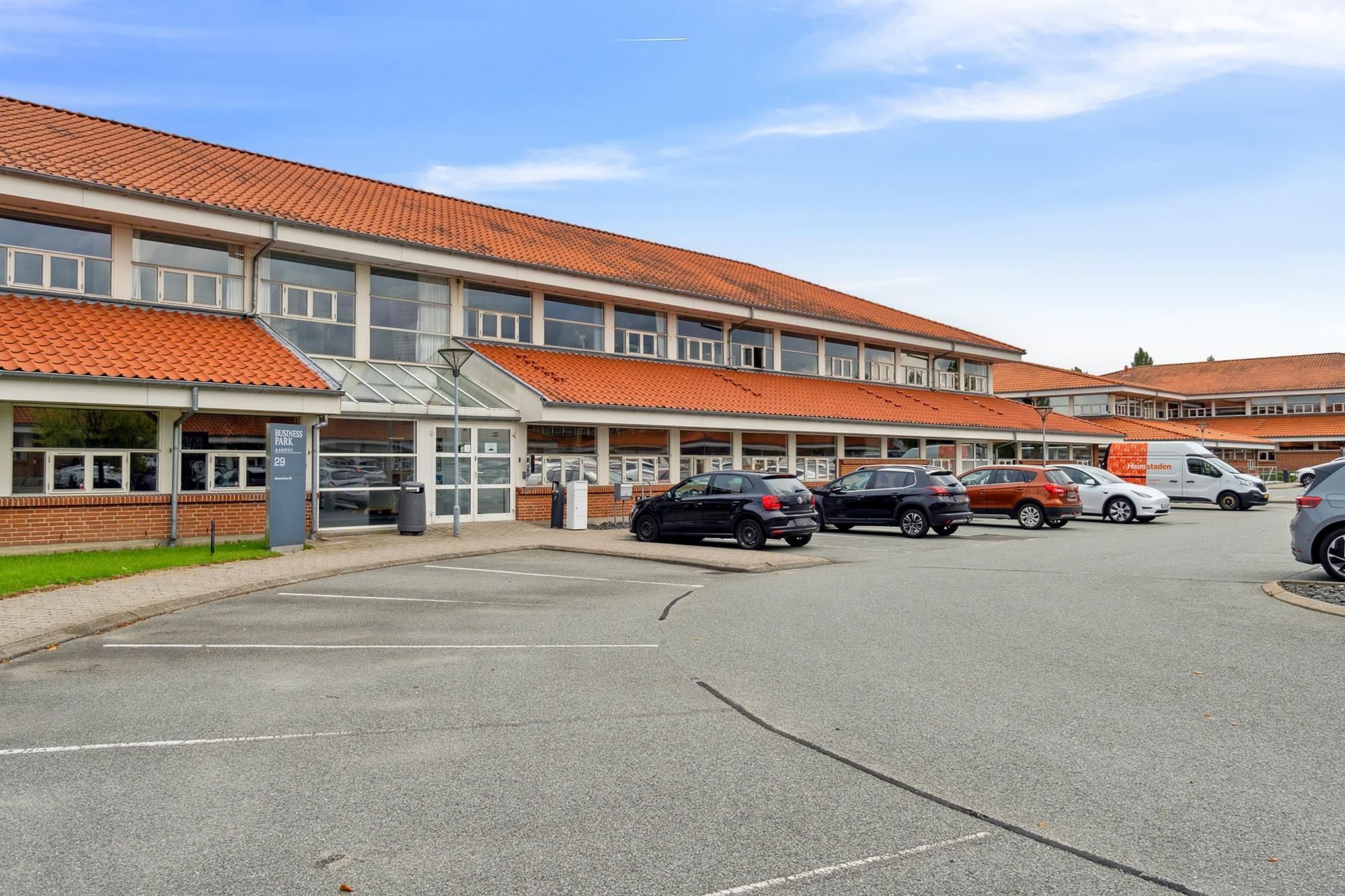 Moderne erhvervspark med røde tag og glasvinduer -Parkeringsplads med flere biler -Forretningscenter med mange kontorer