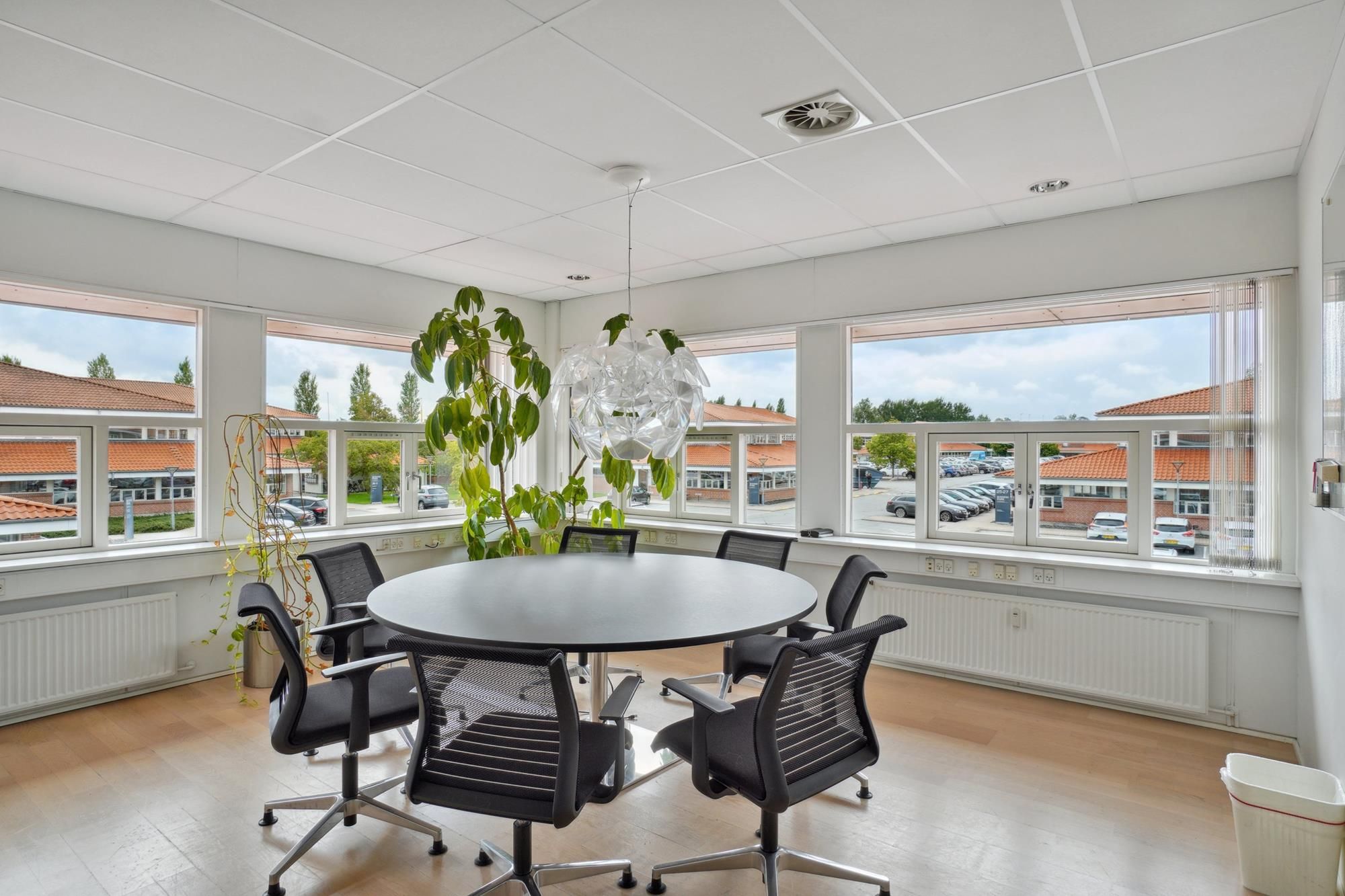 Moderne mødelokale med runde bord og stole -Højt til loftet -Store vinduer med udsigt til parkeringsplads og bygninger