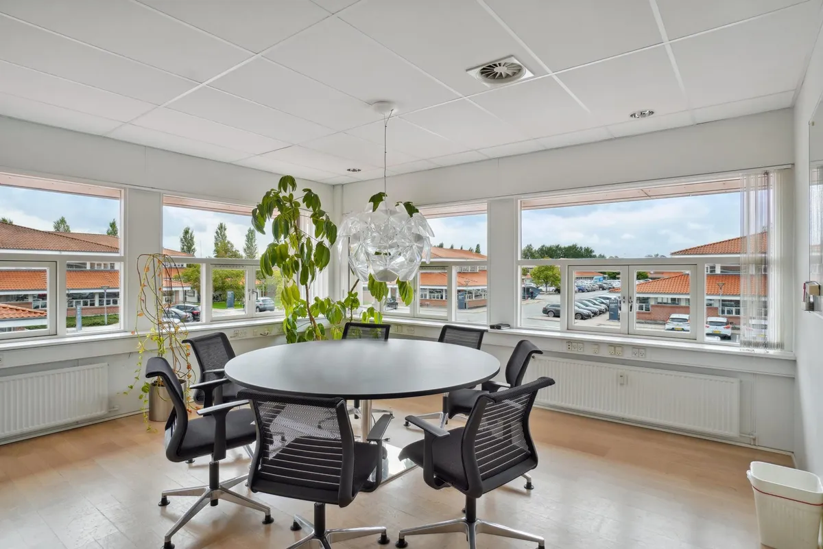 Moderne mødelokale med runde bord og stole -Højt til loftet -Store vinduer med udsigt til parkeringsplads og bygninger