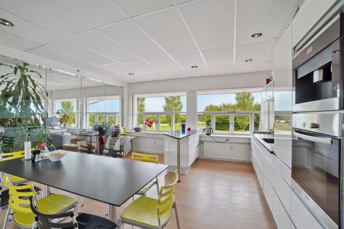 Moderne køkken med højt loft, stort vindue og stolpe med flag og lysegul stol og lysegul bord med frugtskål og servietter