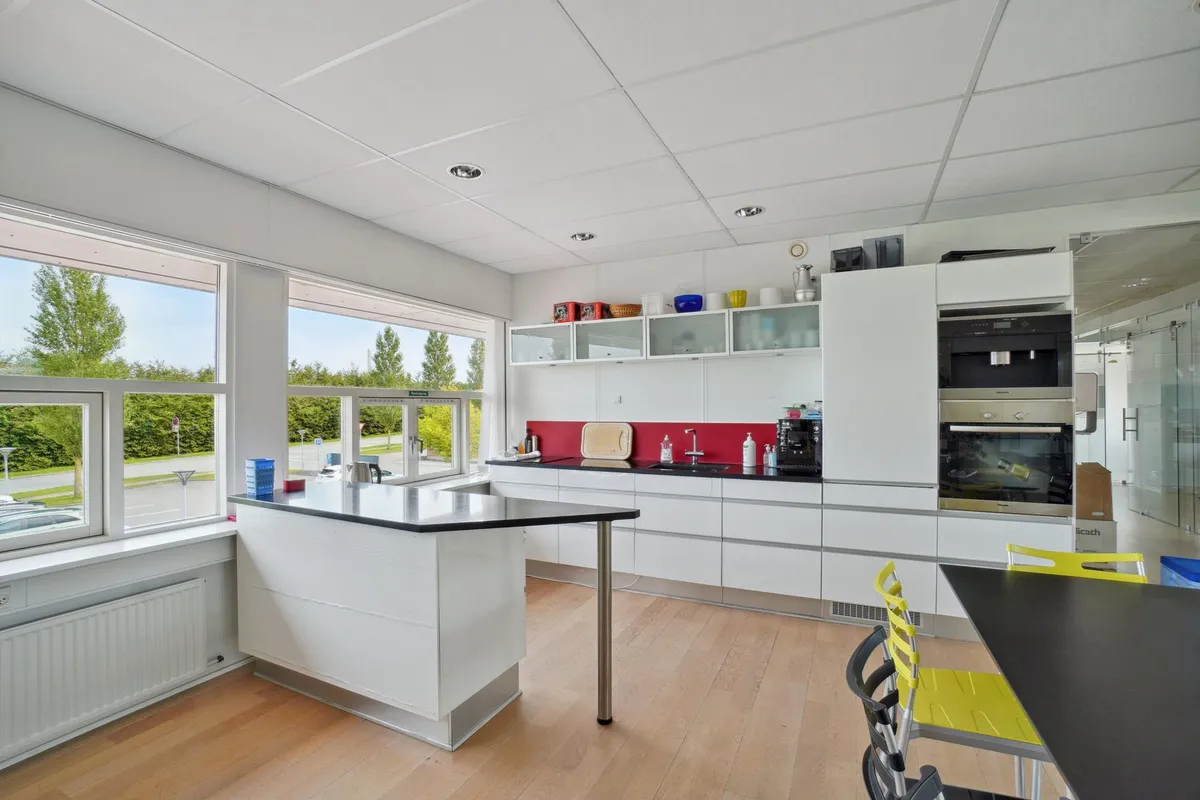 Moderne køkken med højt loft, hvide vægge, gult gulv og store vinduer med udsigt til grønne træer og veje