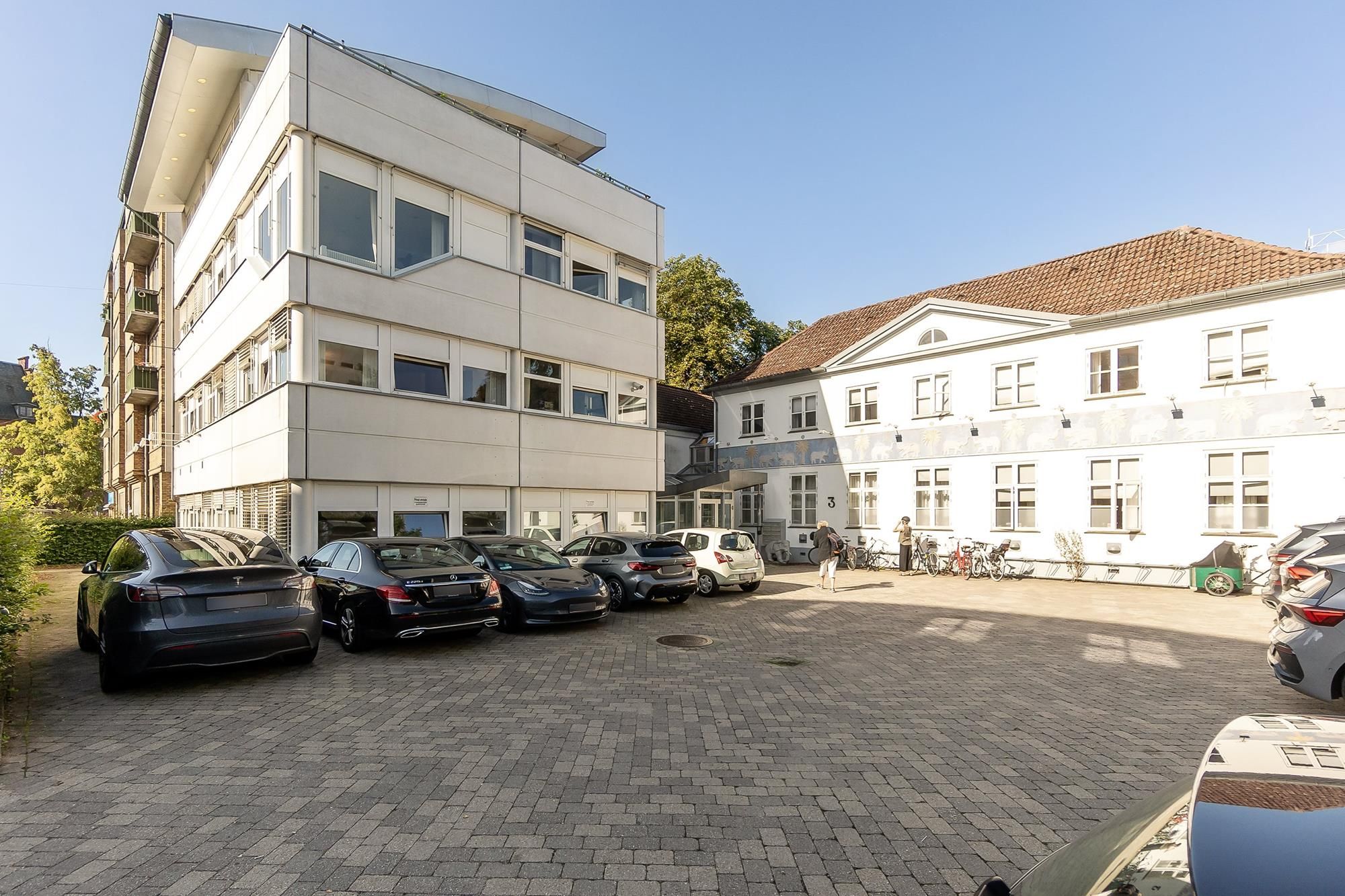 Lejemål med parkeringsplads og tagterrasse. Bygningen er hvid og består af flere lejligheder og et stort parkeringsområde.