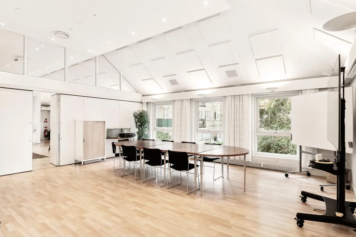 Et moderne mødelokale med hvide vægge og trægulv. Rundt om er der flere lyse, hvide loftsreflekser. Væggen er dekoreret med