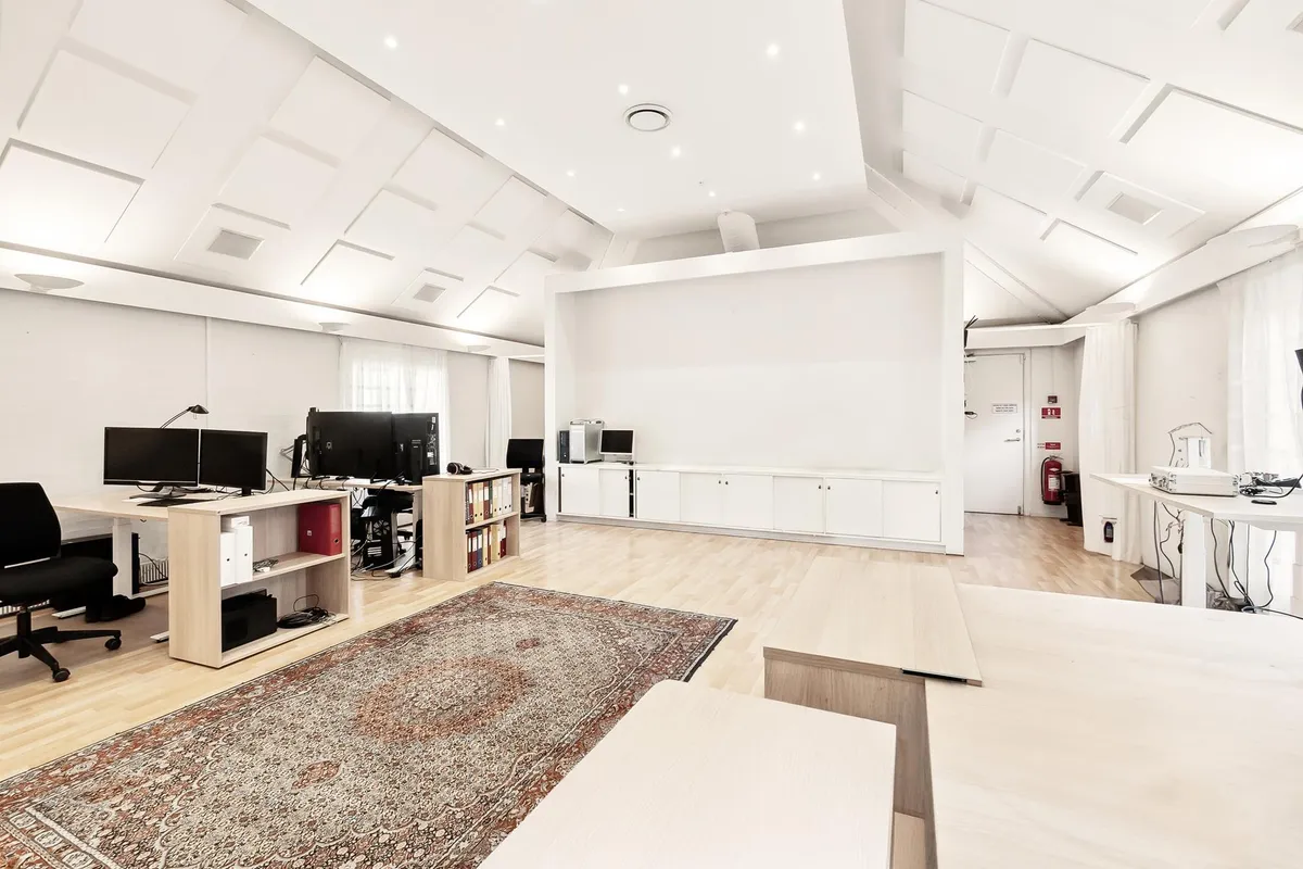 Luksuskontor med lyse vægge og trægulve, møbler og to skærme, højttalere og en orientalsk tæppe på gulvet