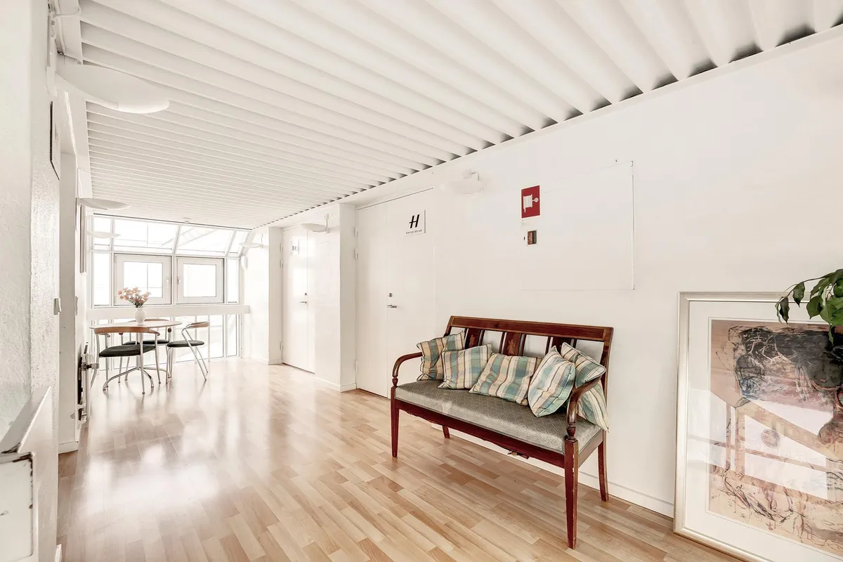 Moderne interiør med hvidt loft, trægulv og lyse møbler samt kunstværk og plante i ramme