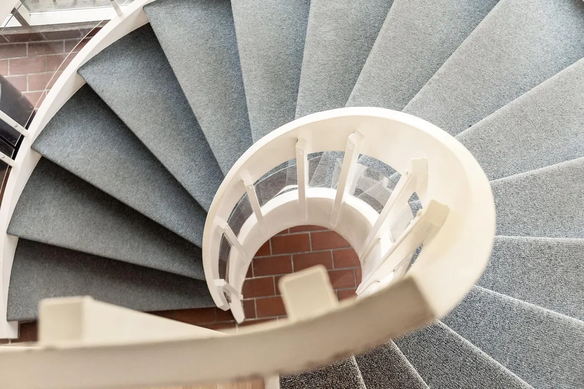 Moderne hvide trapper med glastrin og høj kvalitet. Grå gulvbelægning på alle trin. Rød mursten og gulvtæppe på trappebunden.