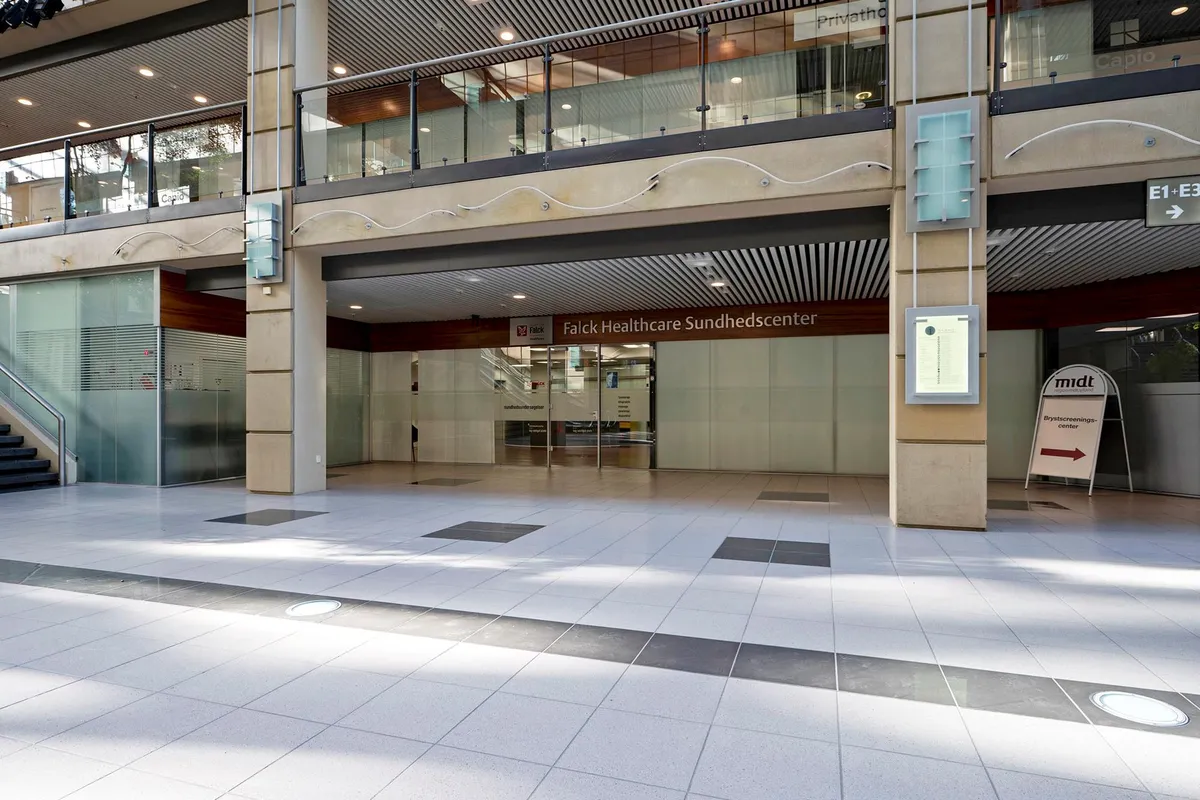 På Falk Healthcare Sundhedscenter i Aarhus ses et stort og velholdt område med glasvægge og en ren lobby med hvide og sorte