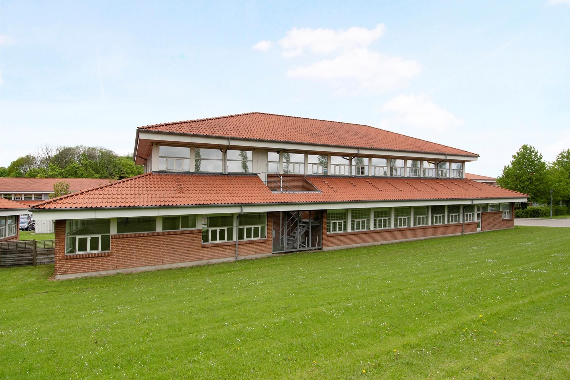 Nyrenoveret og velplejet bygning med rødt tag og glasvinduer på grøn plæne med parkerede biler og park