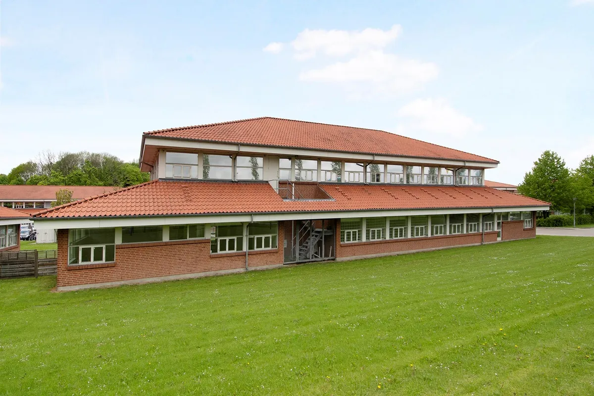 Nyrenoveret og velplejet bygning med rødt tag og glasvinduer på grøn plæne med parkerede biler og park