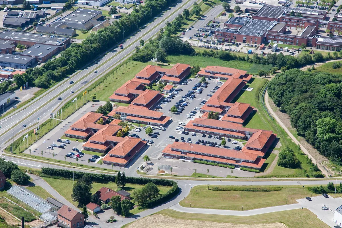 Bygningskompleks med parkeringsplads og grønne omgivelser i Aarhus med flere biler og bygninger i baggrunden