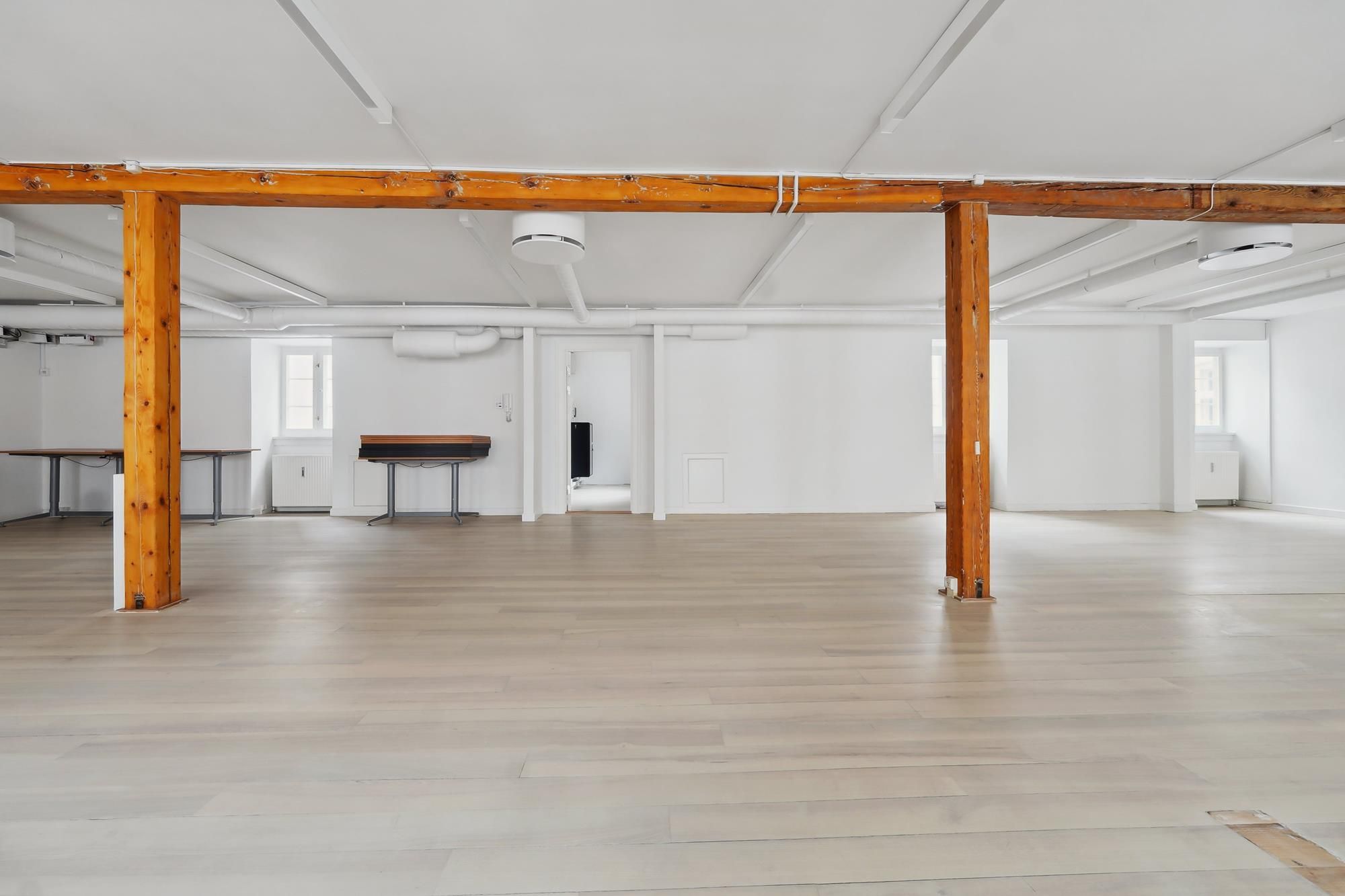 En stor, lyse lokale med hvidt loft, hvide vægge og trægulve samt høje træsøjler fordelt rundt i rummet