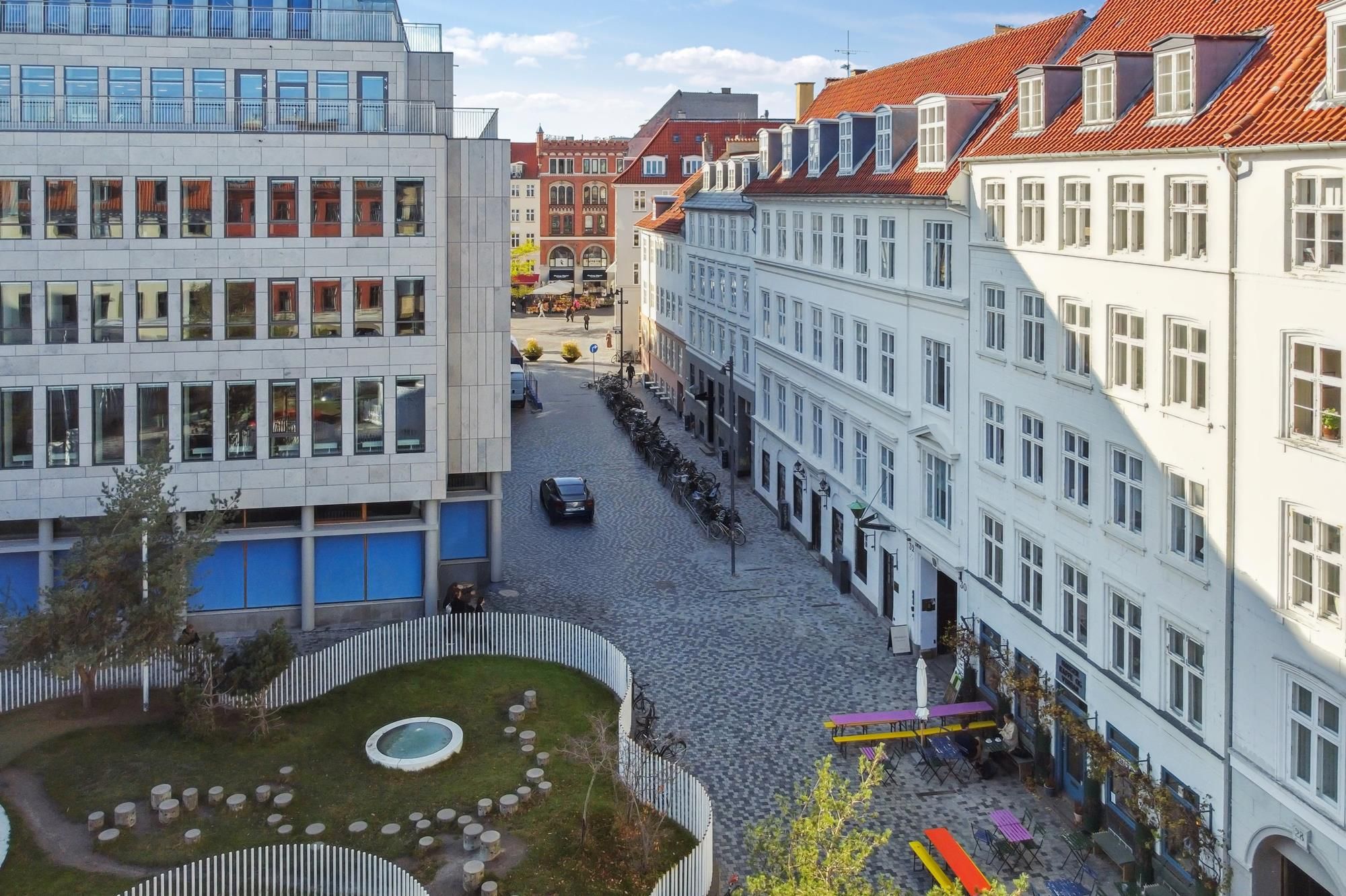 Kontorbygninger med røde tag og hvide facader på Hauser Plads med en parkeringsplads og cykelstilladser
